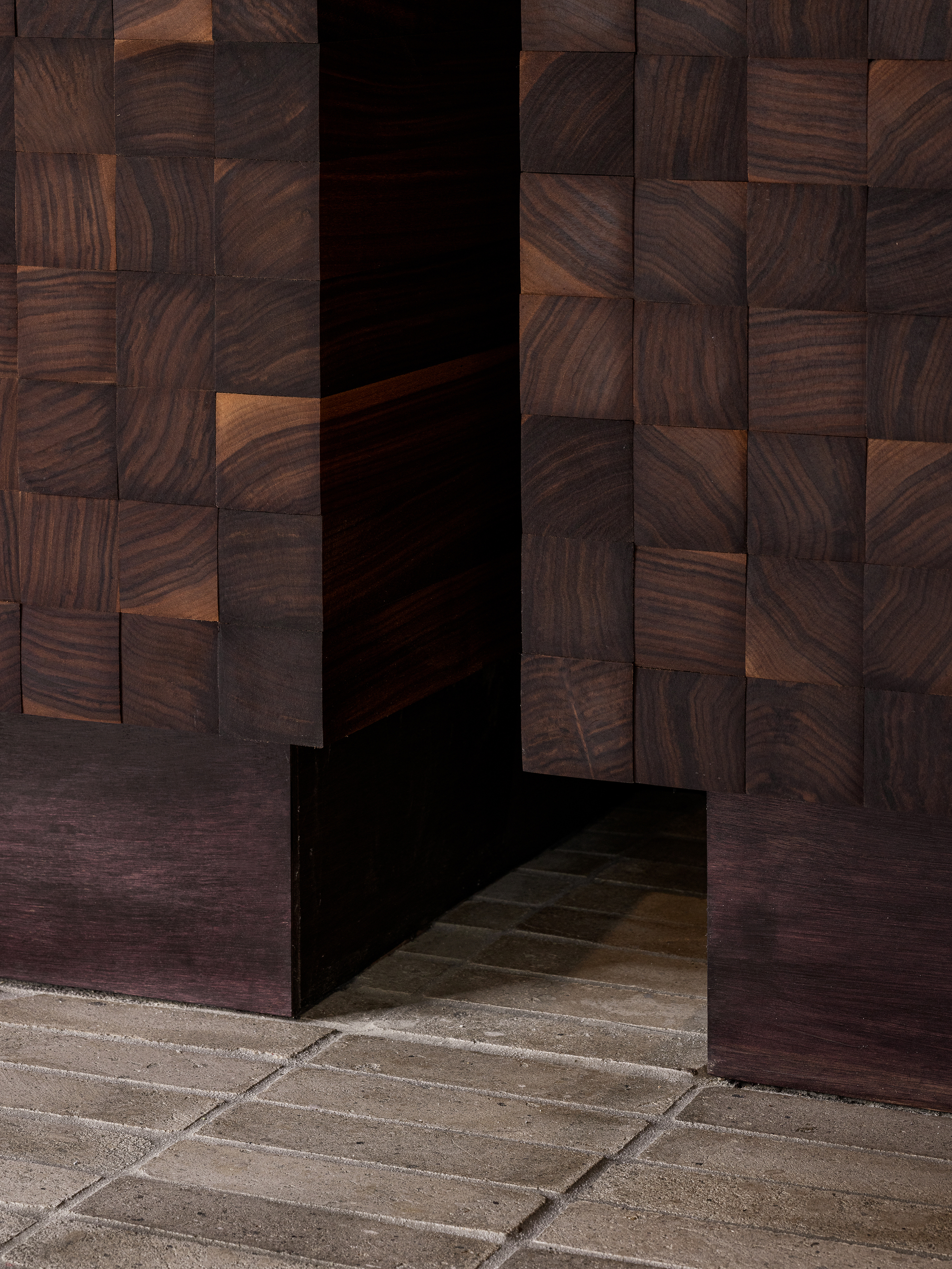 Threshold between stone pavers and dark walnut mosaic wall panels framing a recessed doorway