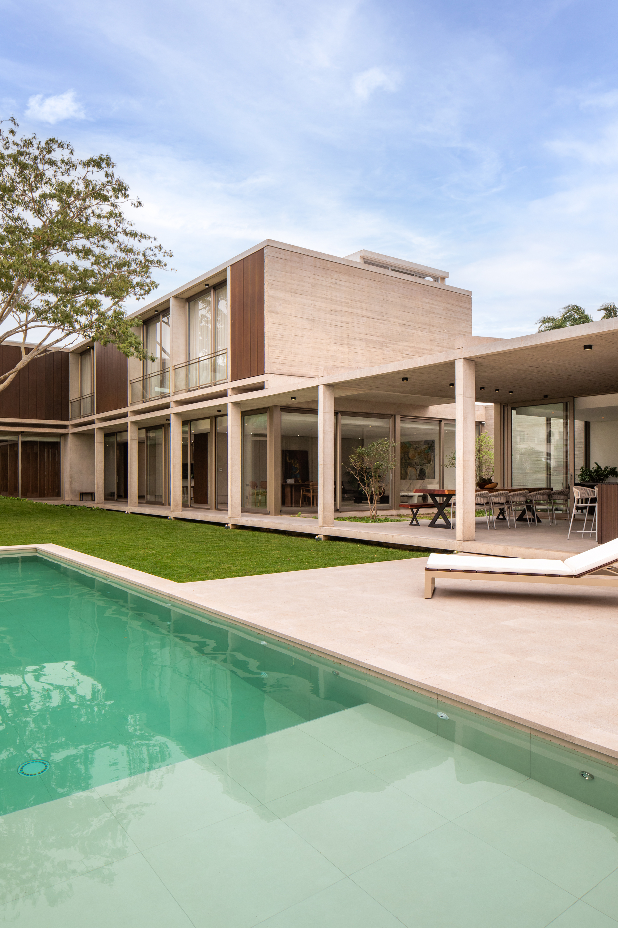 Rear elevation with pool, covered terrace with columns, and timber-clad upper volume framing the lawn