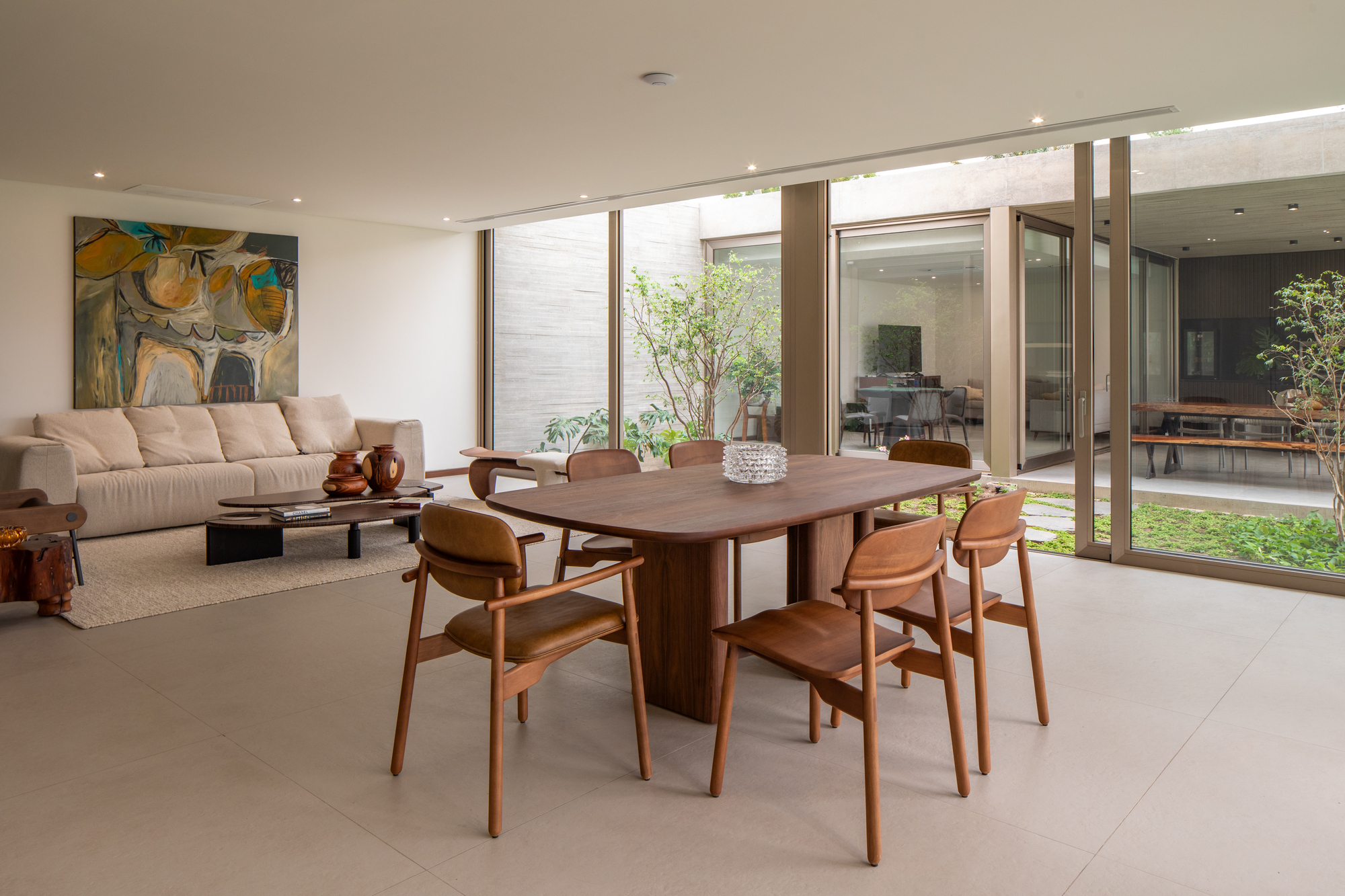 Open-plan dining and living area with timber table, terrazzo flooring, and views to planted courtyards