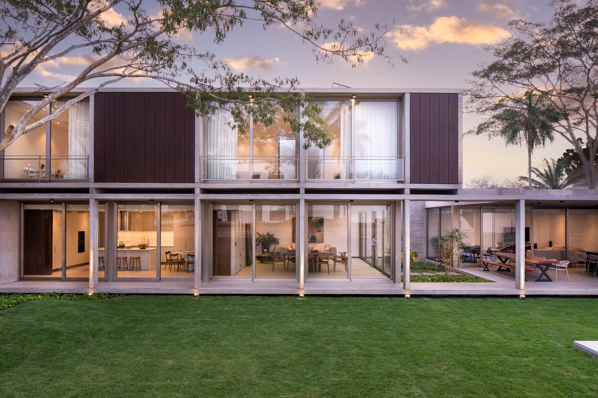 Two-storey glass and timber-clad facade framed by eucalyptus trees under an evening sky