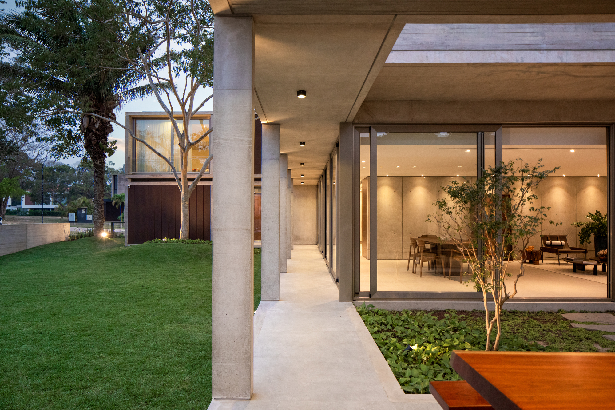 Covered walkway with concrete columns leading past a planted courtyard at dusk