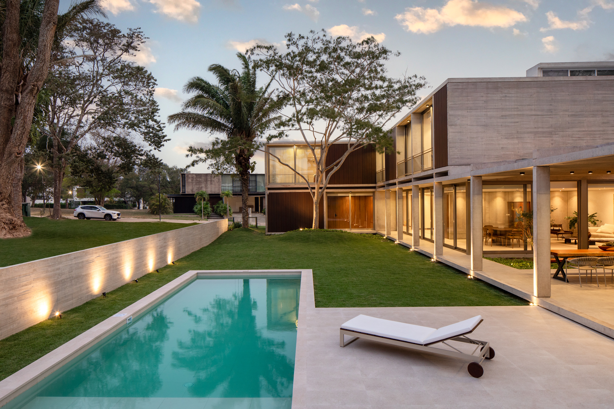 Garden view showing the swimming pool, lawn, and illuminated glass facades at twilight