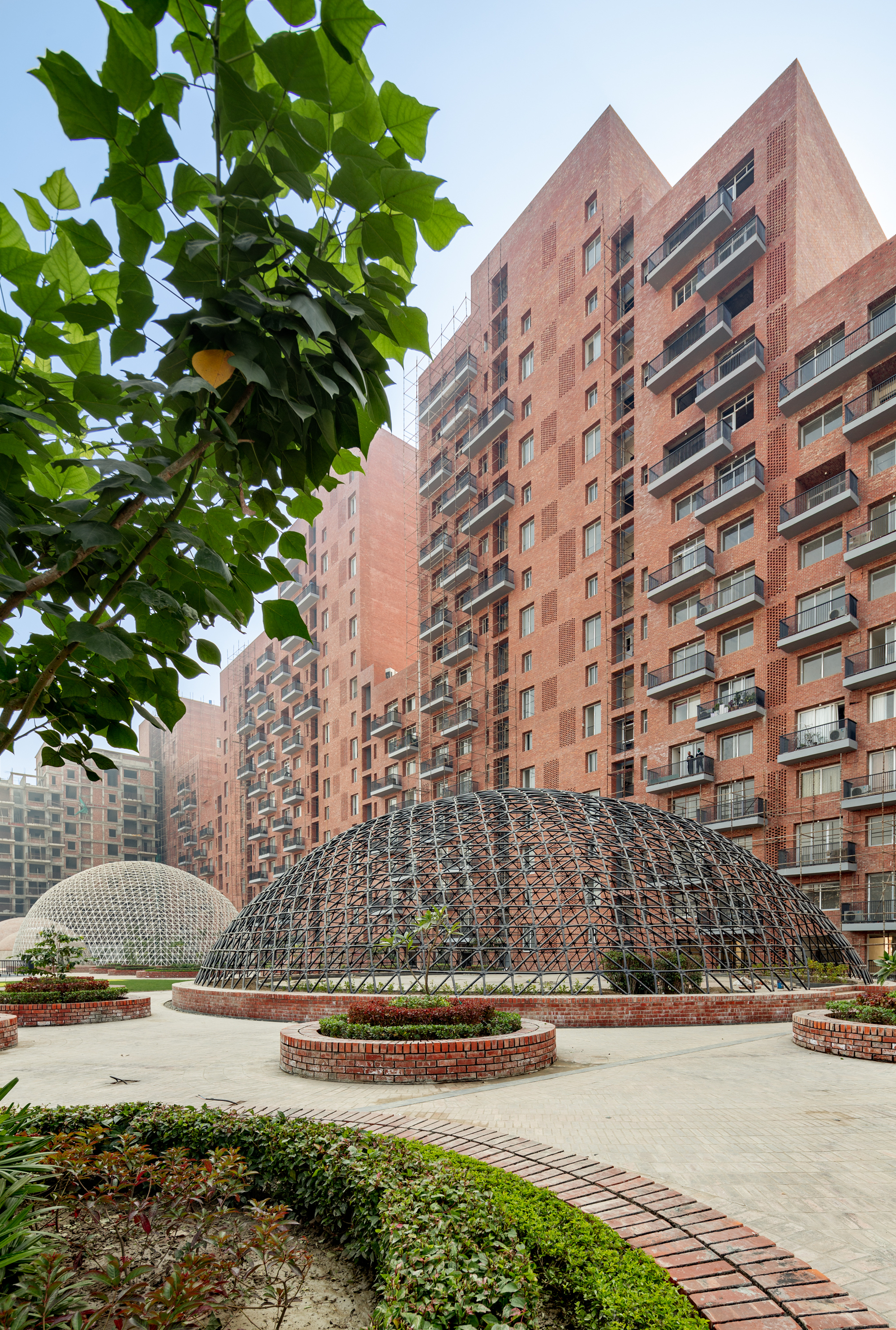 Steel geodesic dome in a courtyard plaza with residential towers and green foliage in the foreground