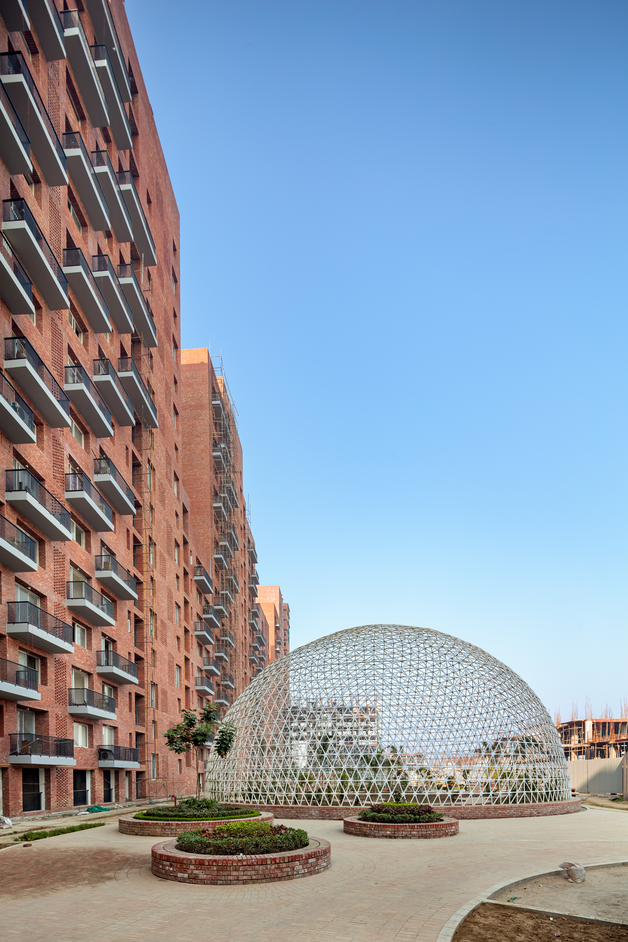 White geodesic dome beside brick towers with circular planted beds in the foreground under clear sky