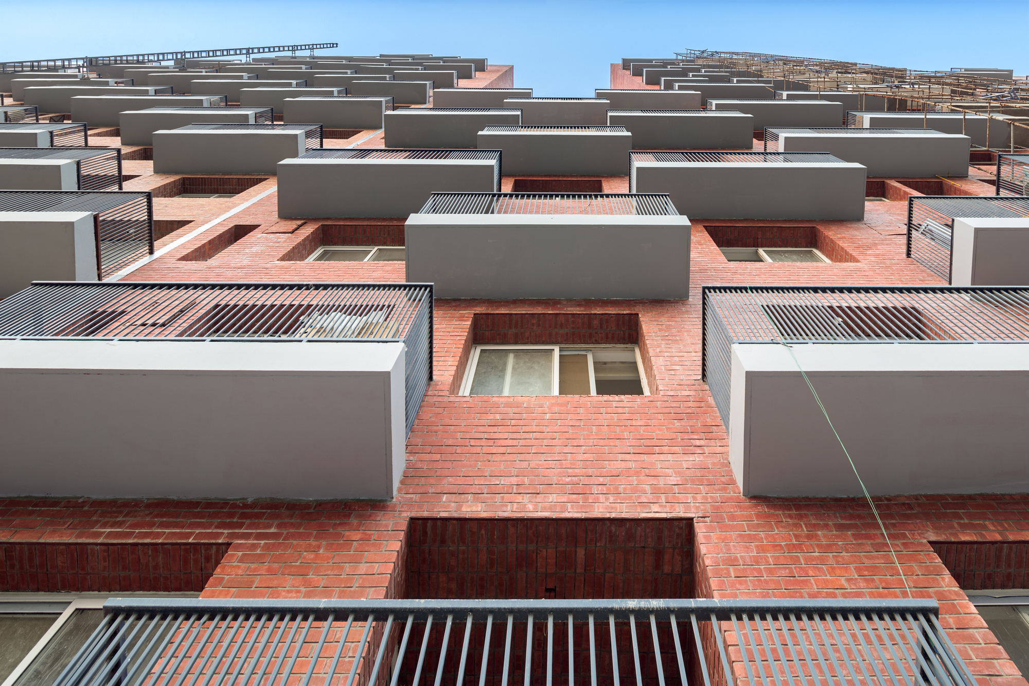 Upward view of the terraced facade showing alternating brick volumes and corrugated metal sunshades under a clear sky