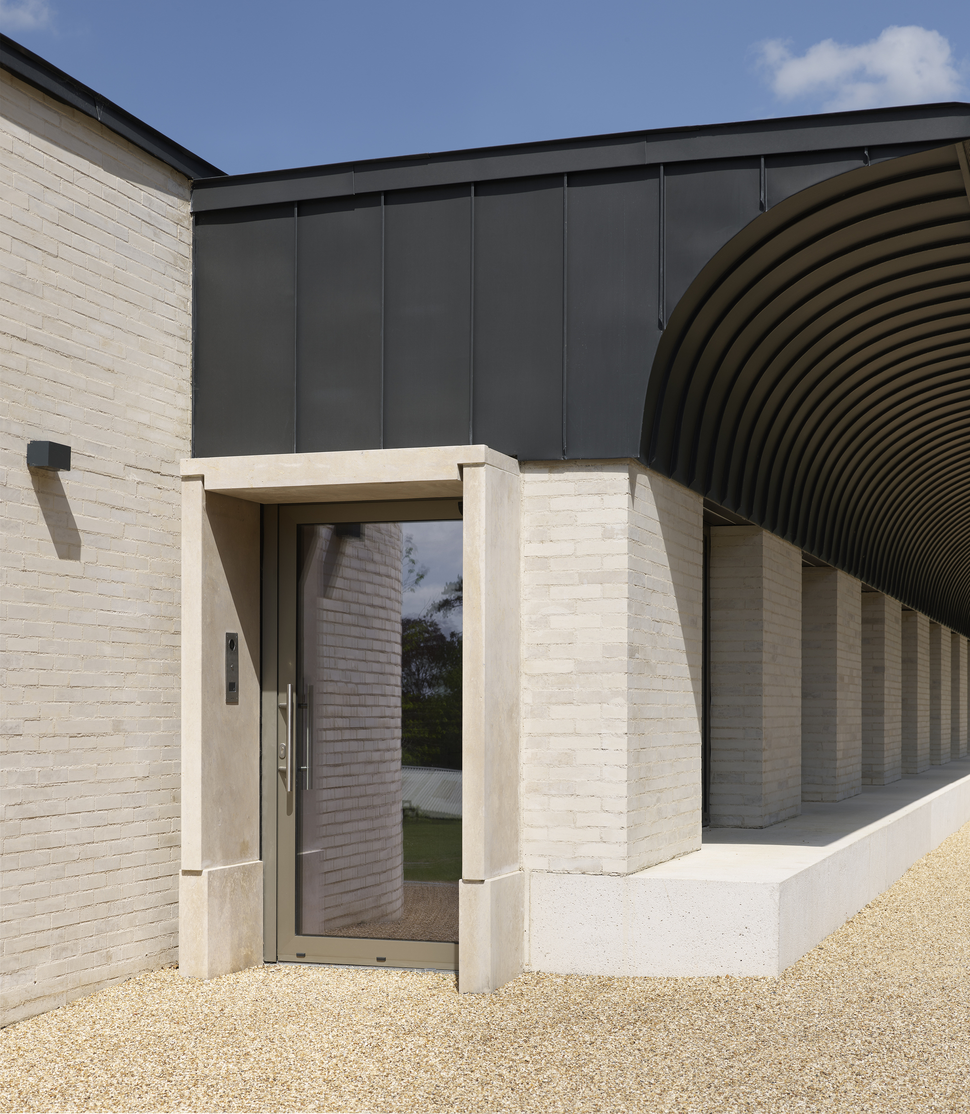 Recessed entrance with cast-concrete frame and dark metal cladding under a blue sky