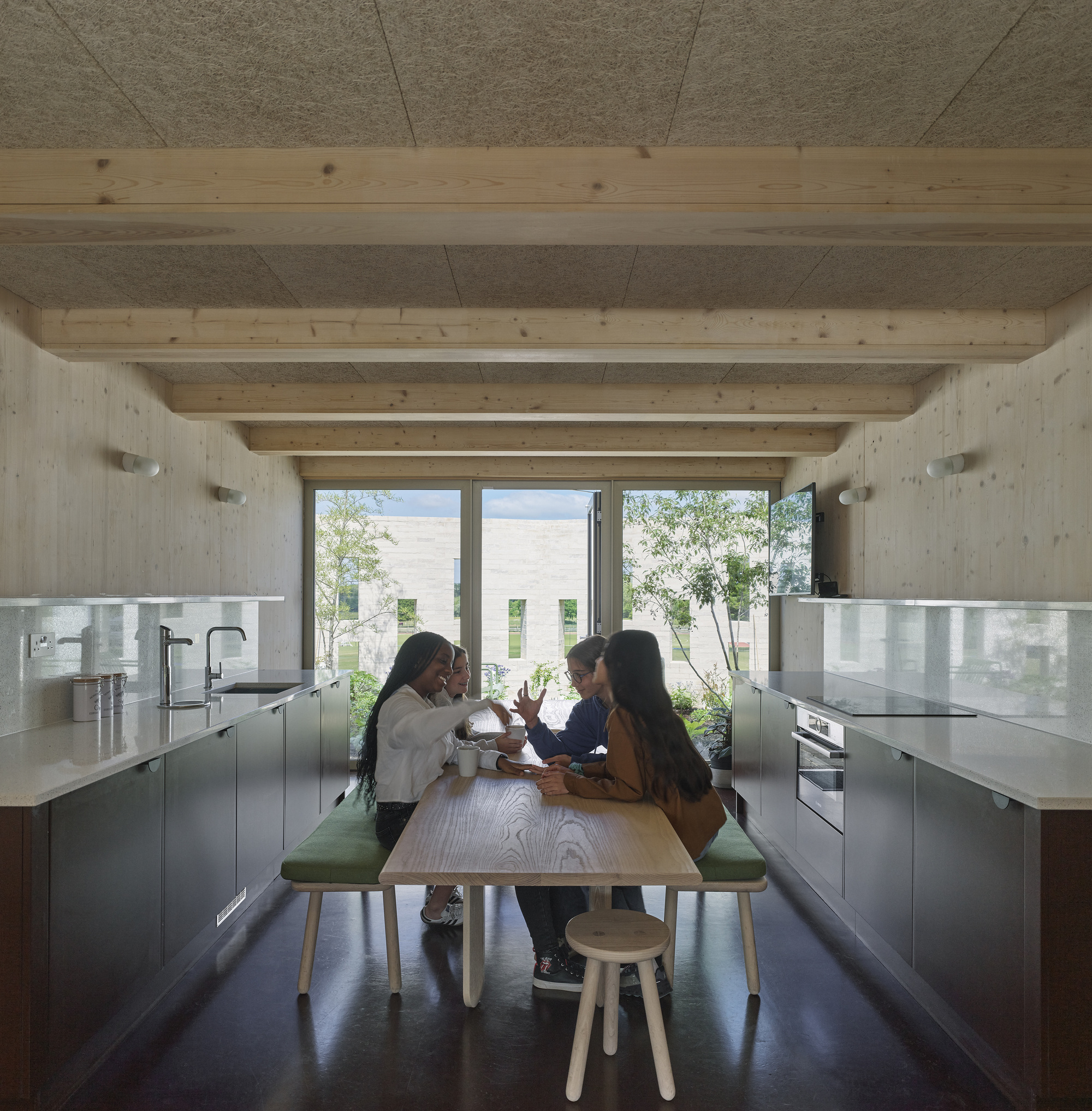 Kitchen with exposed timber beams and three people seated at a table facing courtyard windows