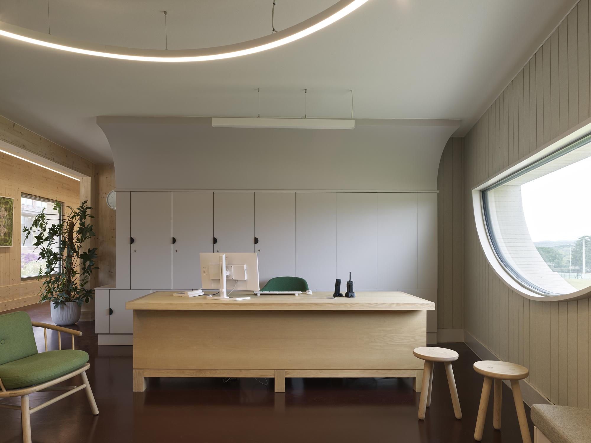 Workspace with circular window and curved ceiling detail lit by recessed linear lighting