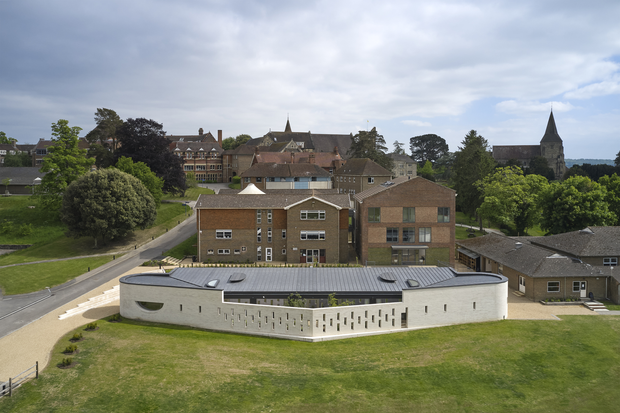 Aerial view of the curved white perforated facade set within a campus of brick buildings