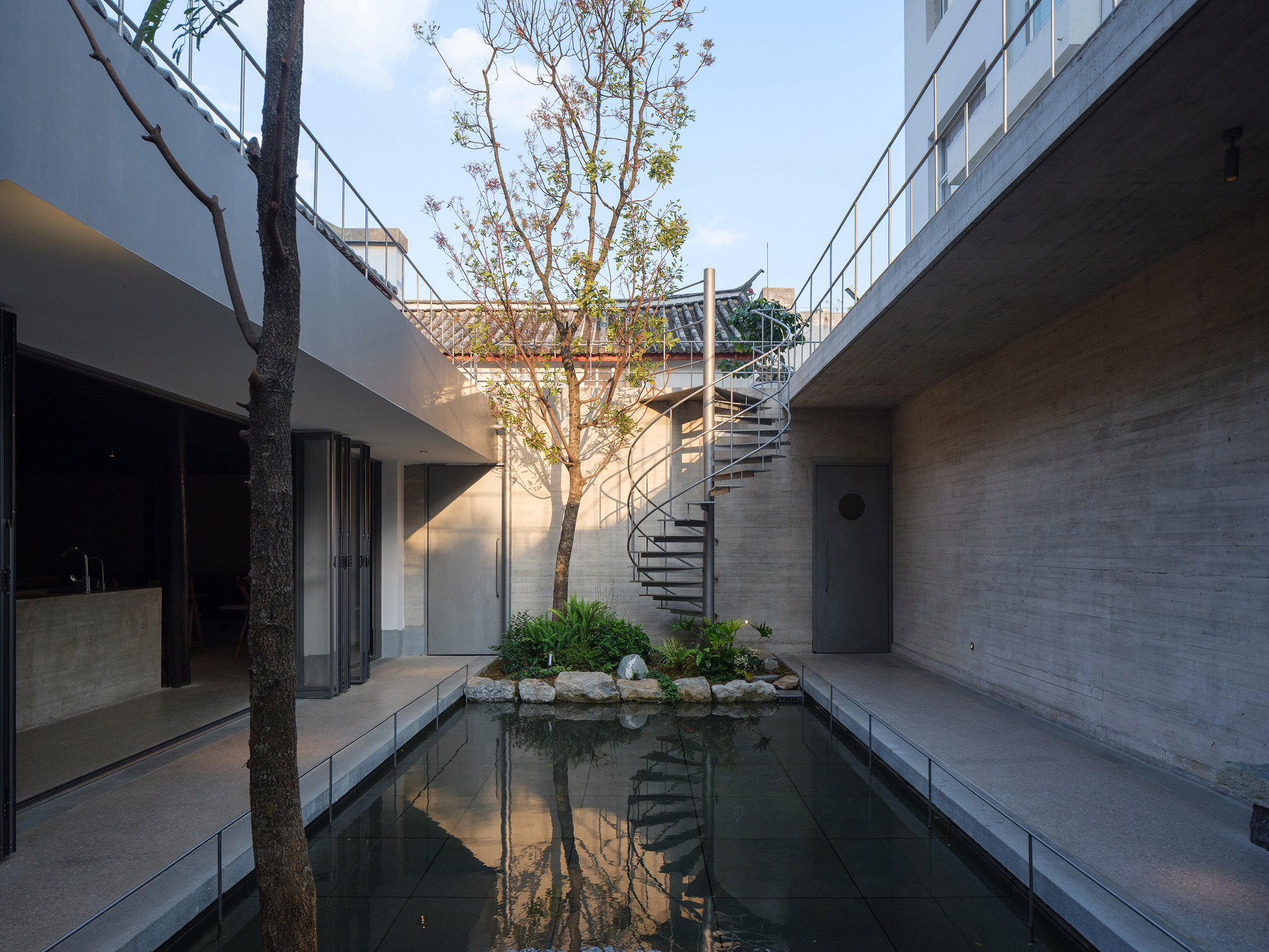 Central courtyard with reflecting pool, spiral staircase, and preserved tree under open sky at dusk