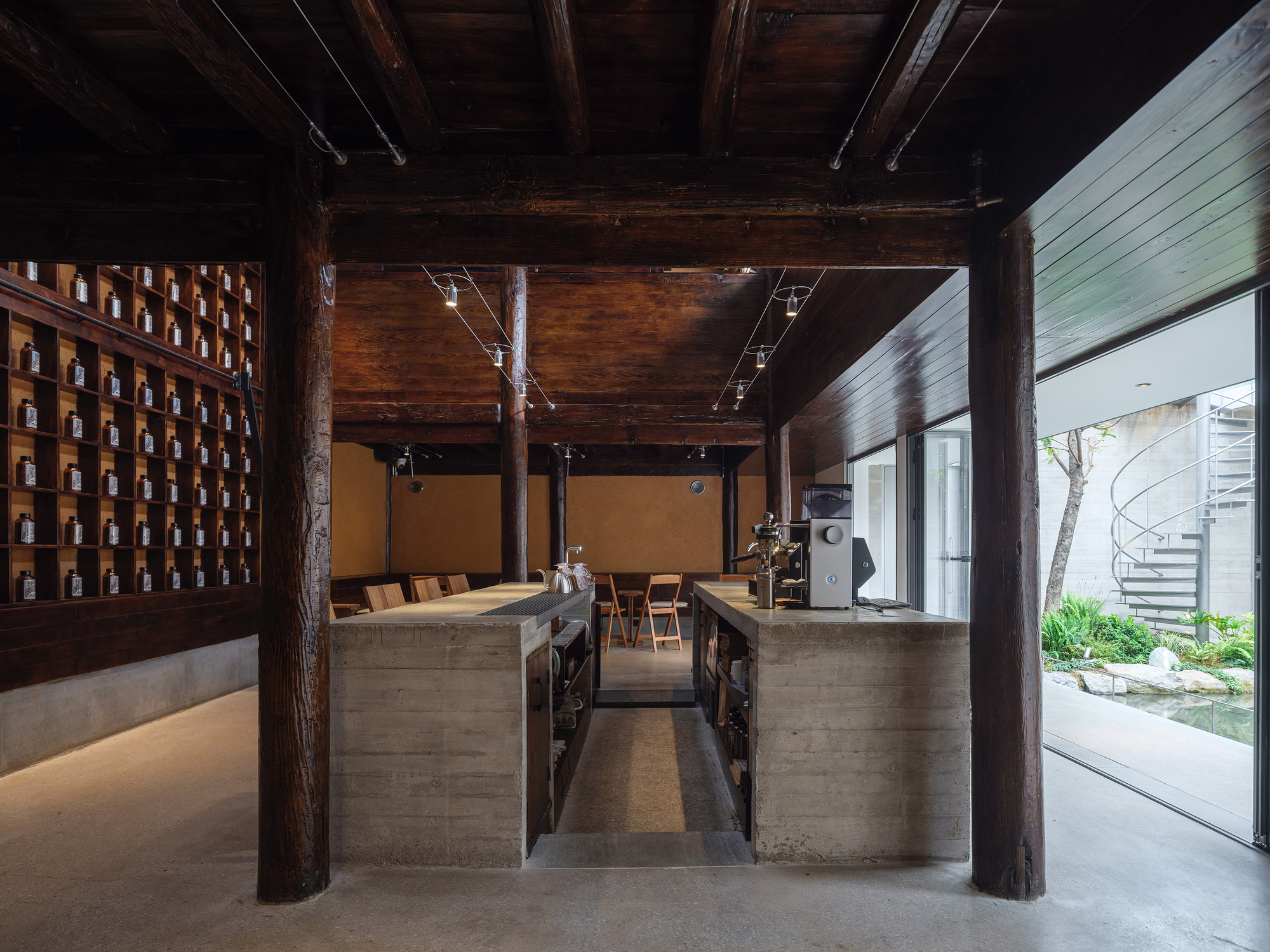 Open kitchen and dining area with timber post-and-beam structure, concrete counters, and view to courtyard