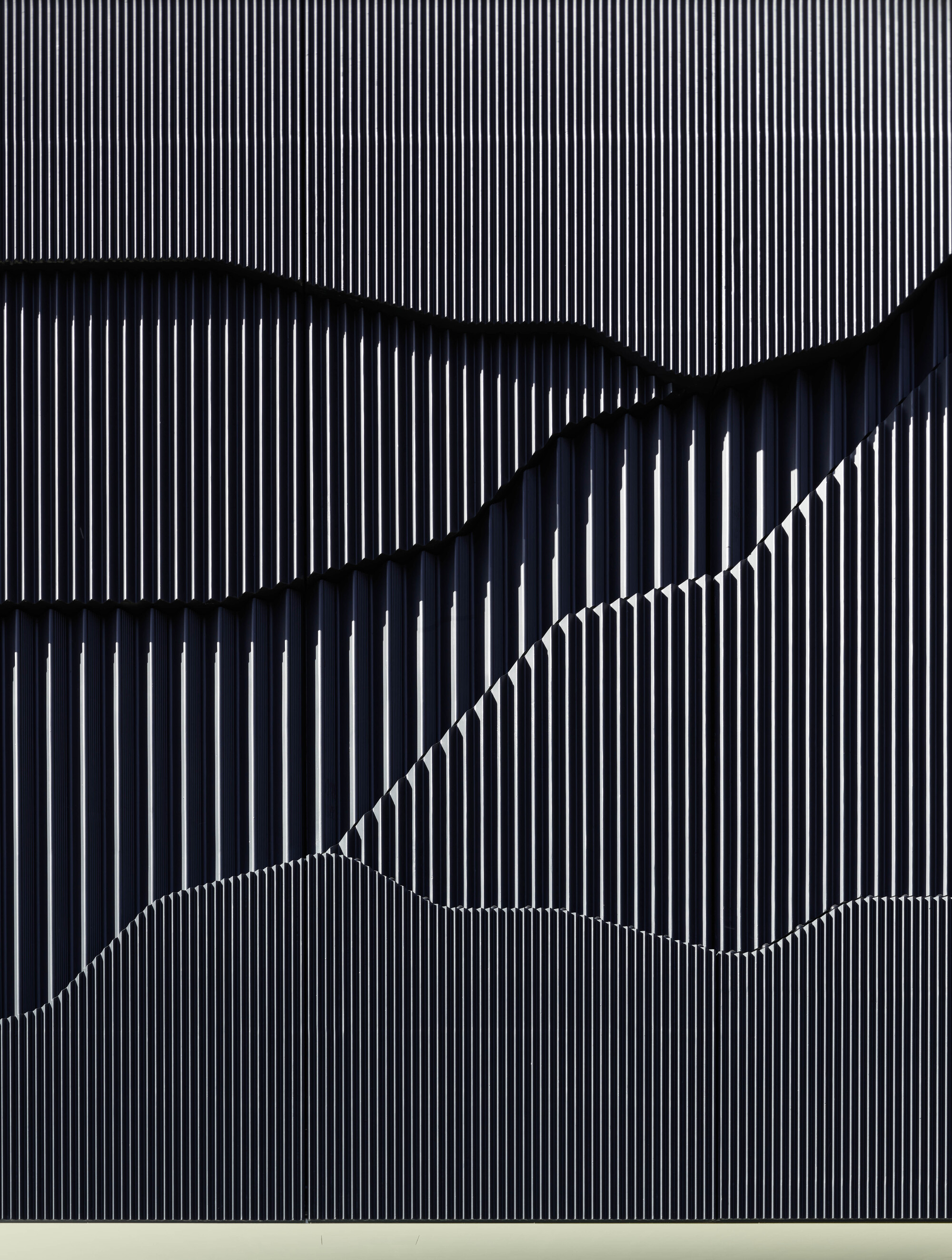 Close-up of vertical metal fin cladding forming wave-like shadows across the facade surface