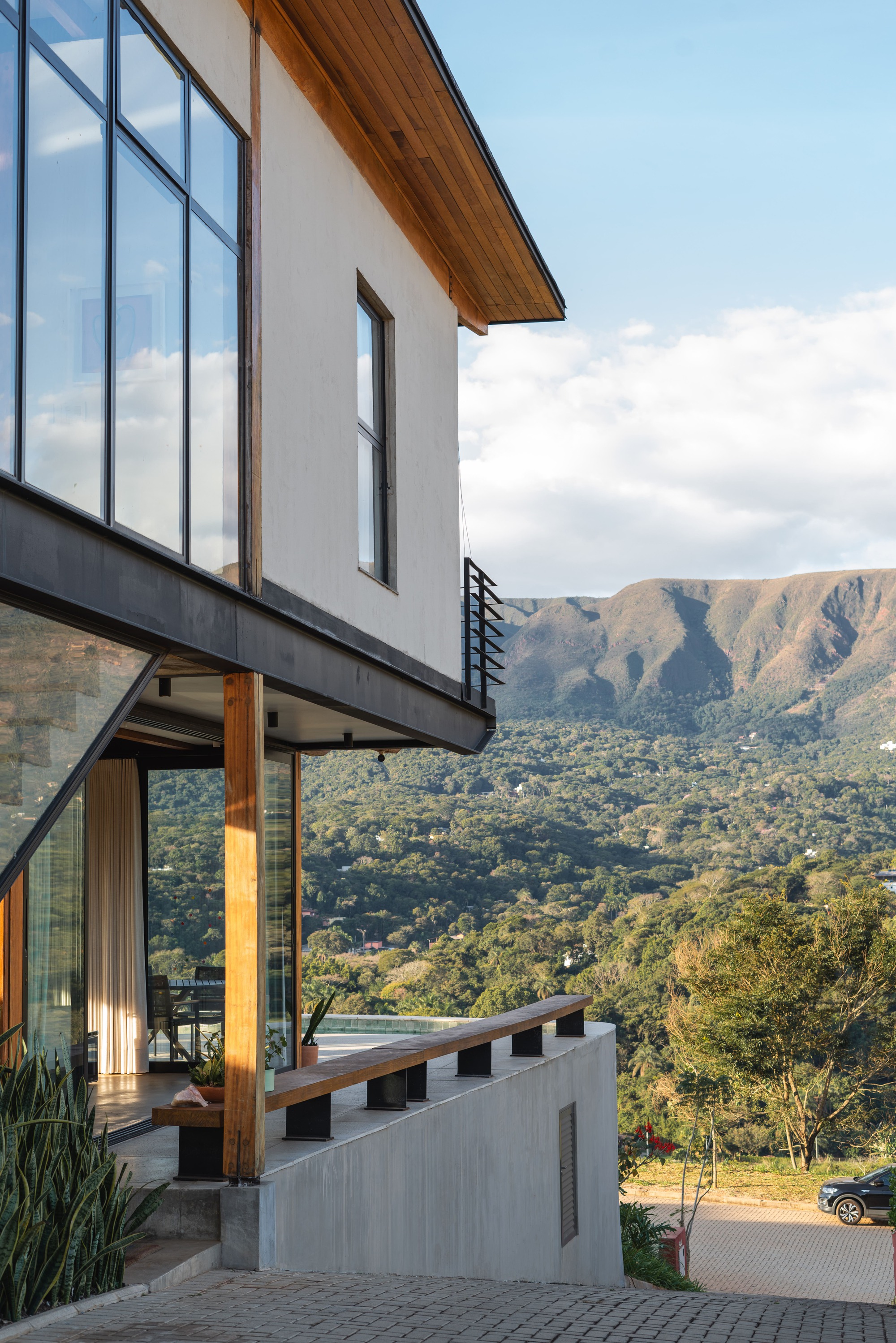 Cantilevered upper volume supported by timber columns with mountain range visible in the distance