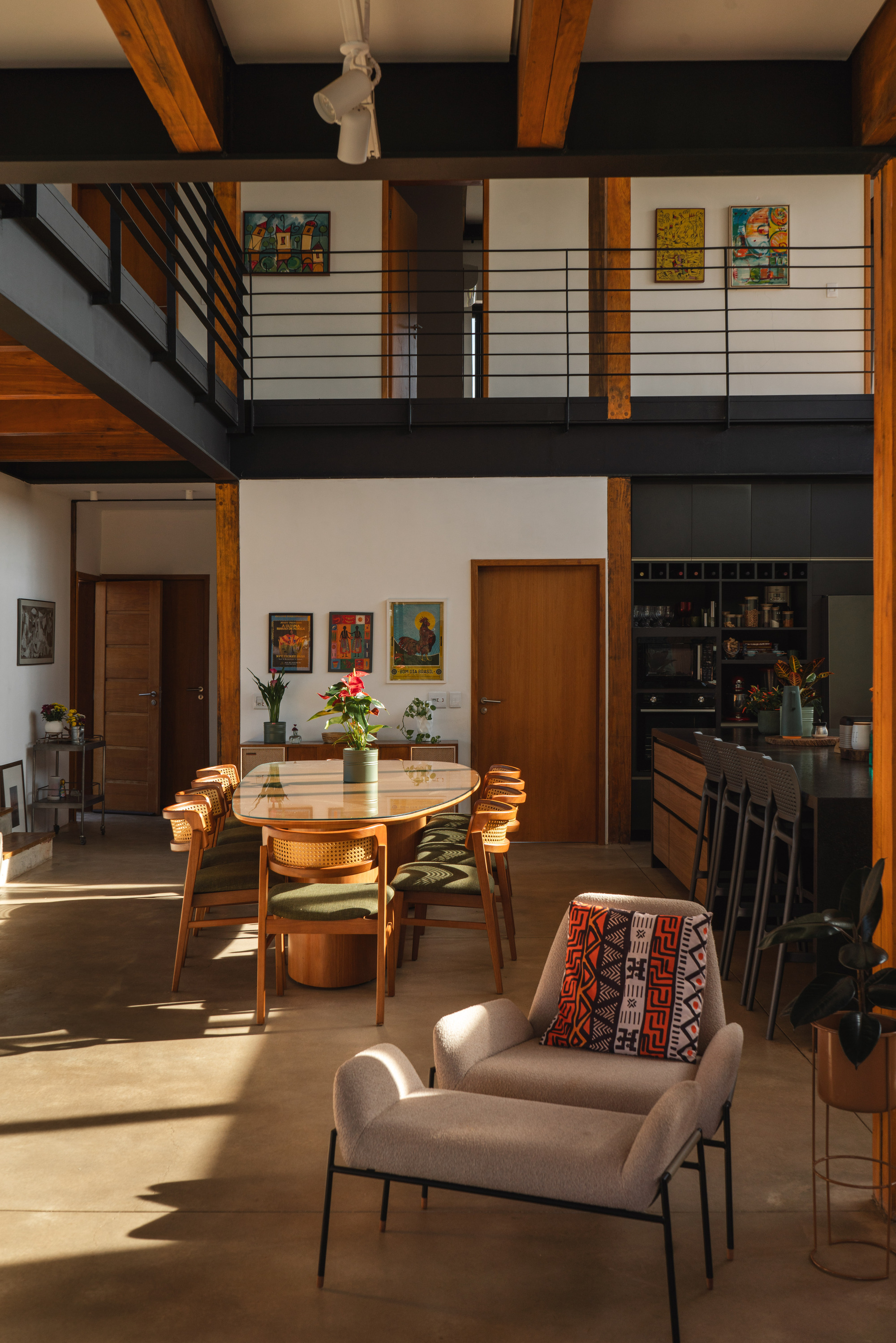 Double-height living space with exposed timber beams, mezzanine balcony and afternoon sunlight on polished floor