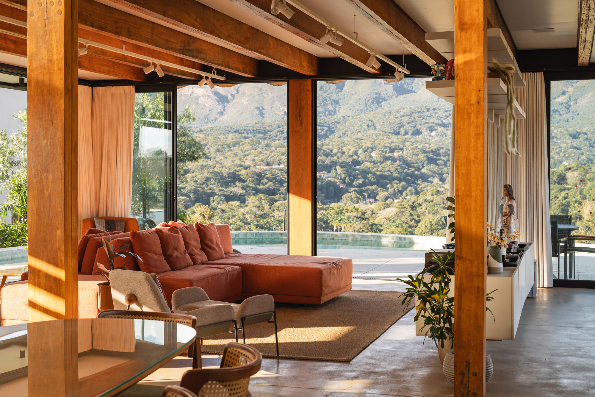 Open living area with exposed timber columns and full-height glazing overlooking infinity pool and hillside