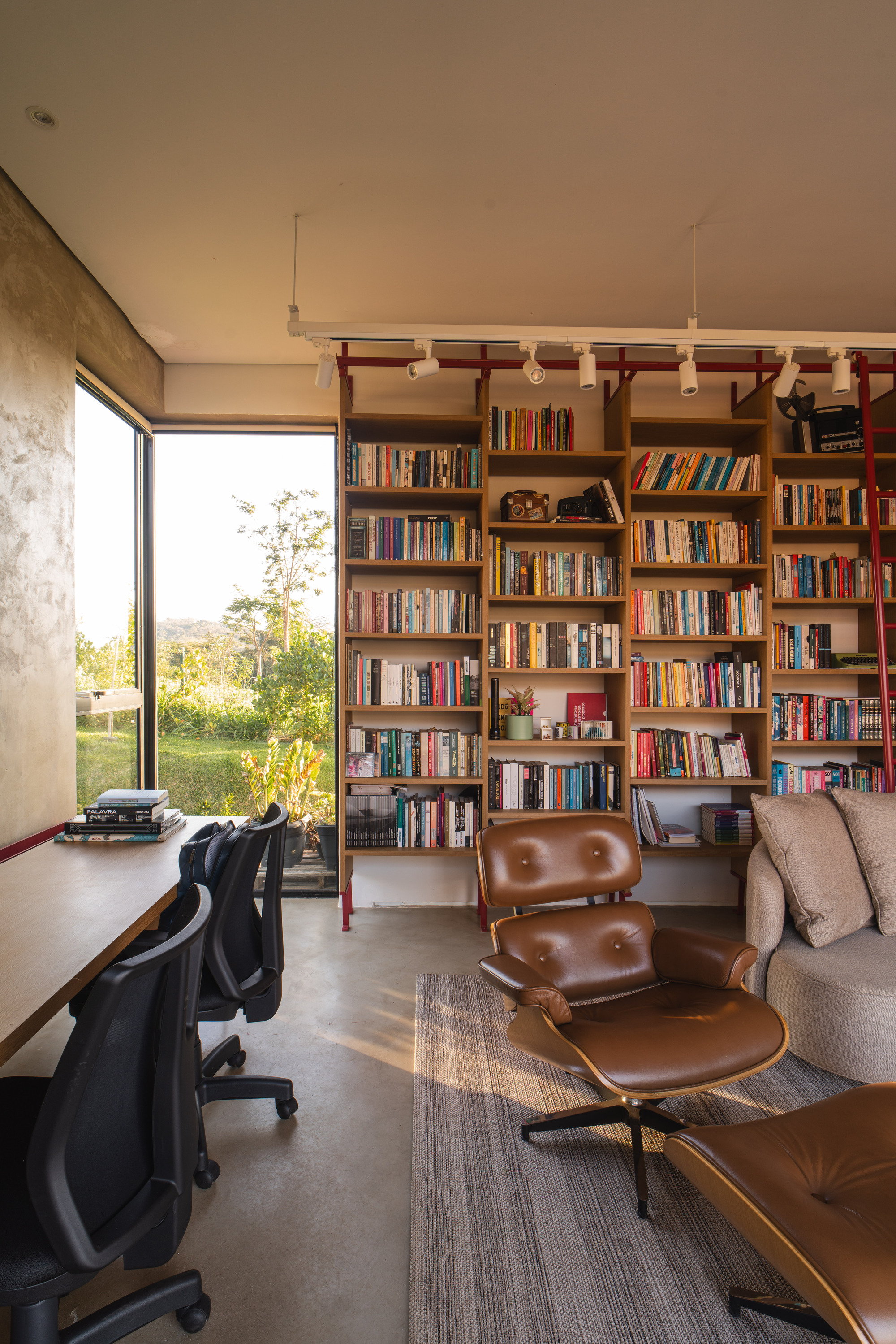 Home office with floor-to-ceiling bookshelves, red steel ladder rail and corner window view