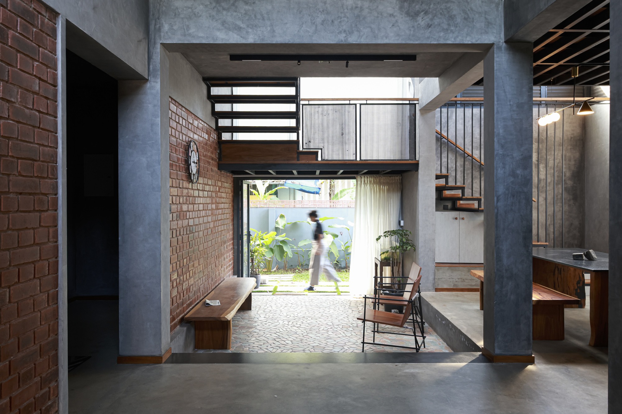 Entry hall with concrete columns and mezzanine bridge framing view to garden with figure walking