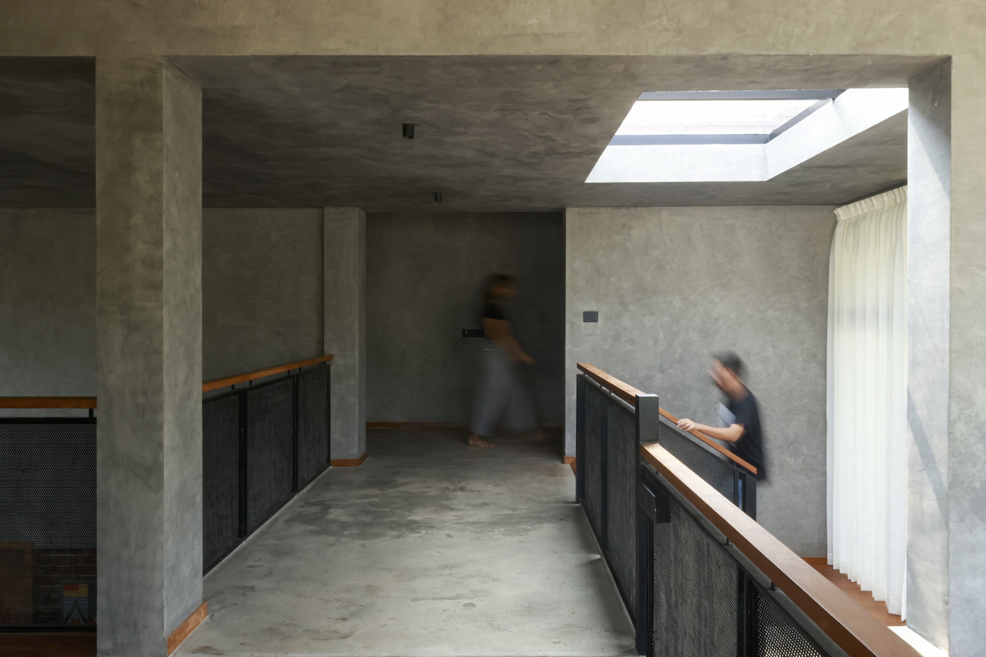 Upper level corridor with concrete ceiling and skylight illuminating two figures in motion