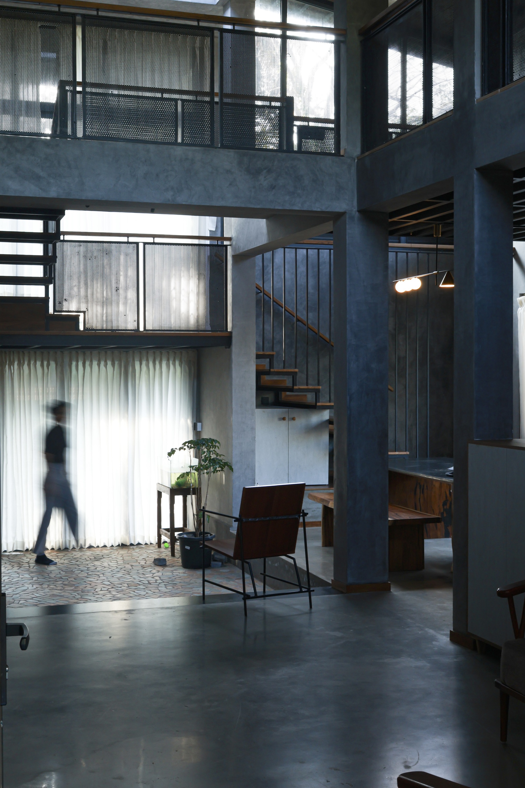 Double-height living space with steel staircase and mezzanine bridges lit by filtered daylight