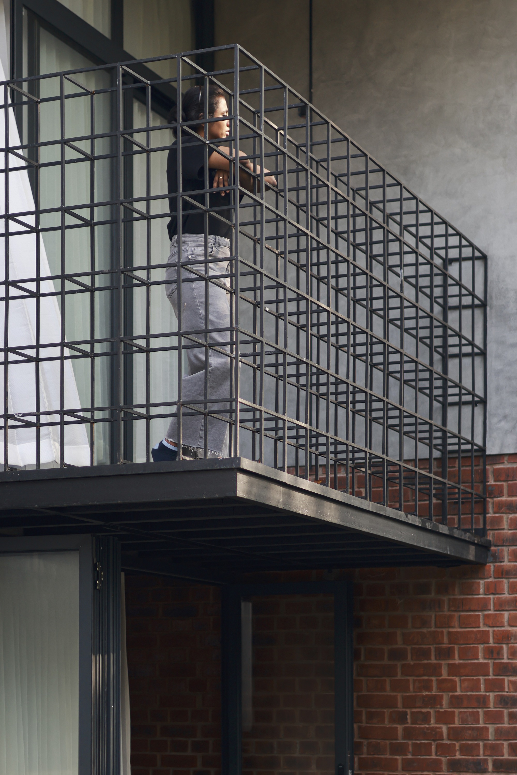 Steel grid staircase with person ascending between concrete slab and brick wall