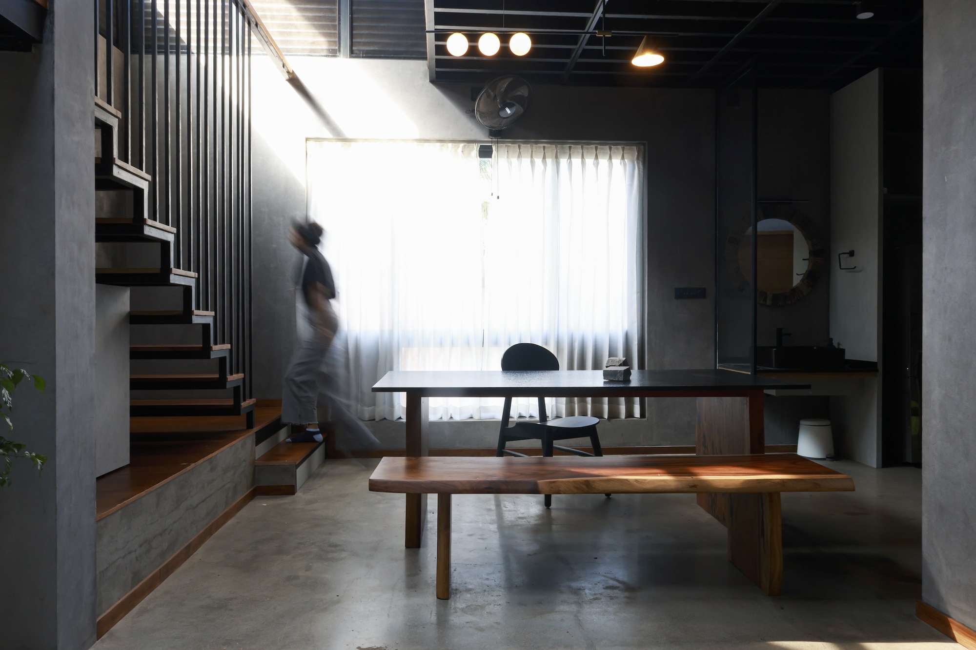 Living space with timber dining table and bench, a figure descending the staircase in motion
