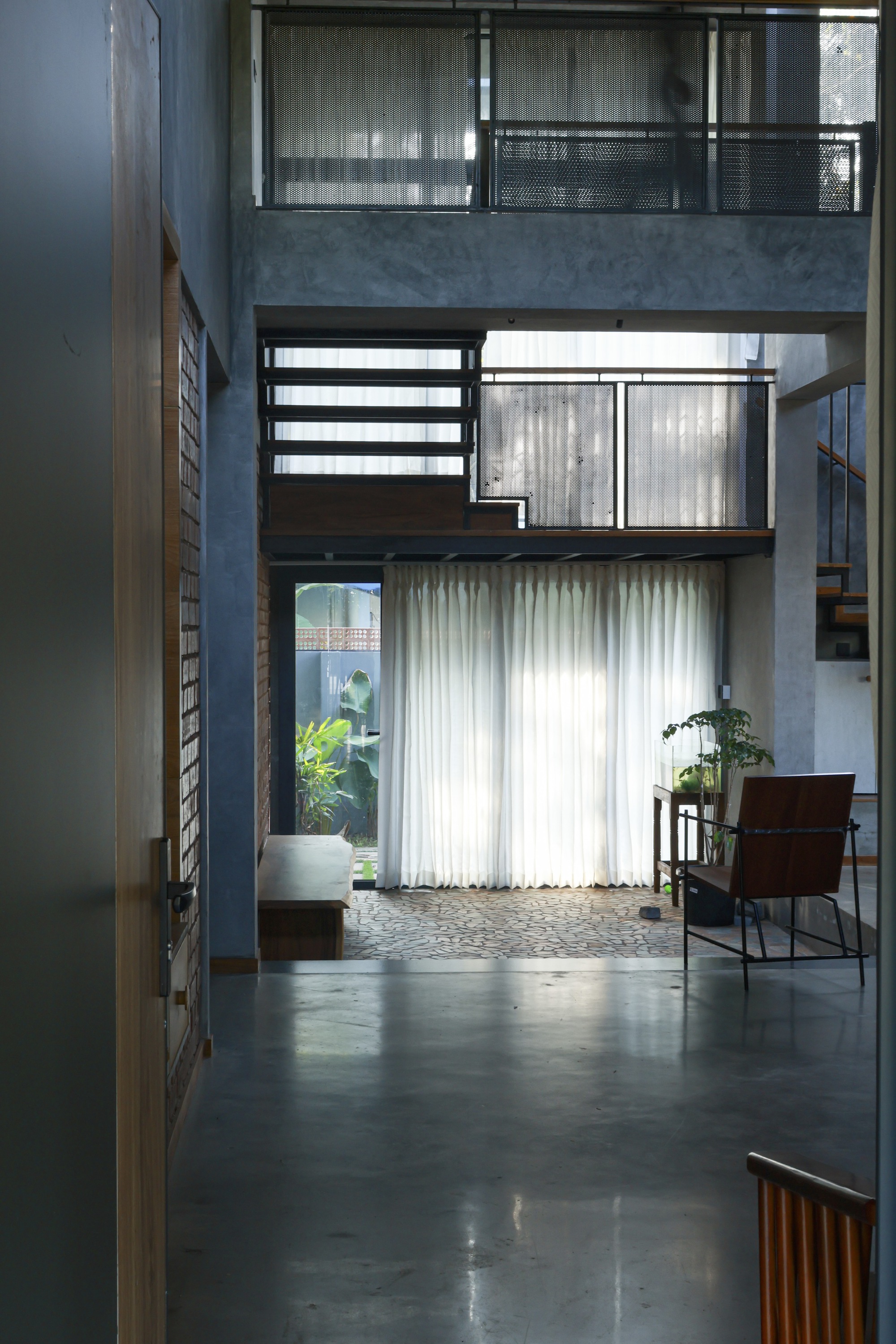 Three-level interior void with stacked balconies, concrete walls, and sheer curtains over polished concrete floors