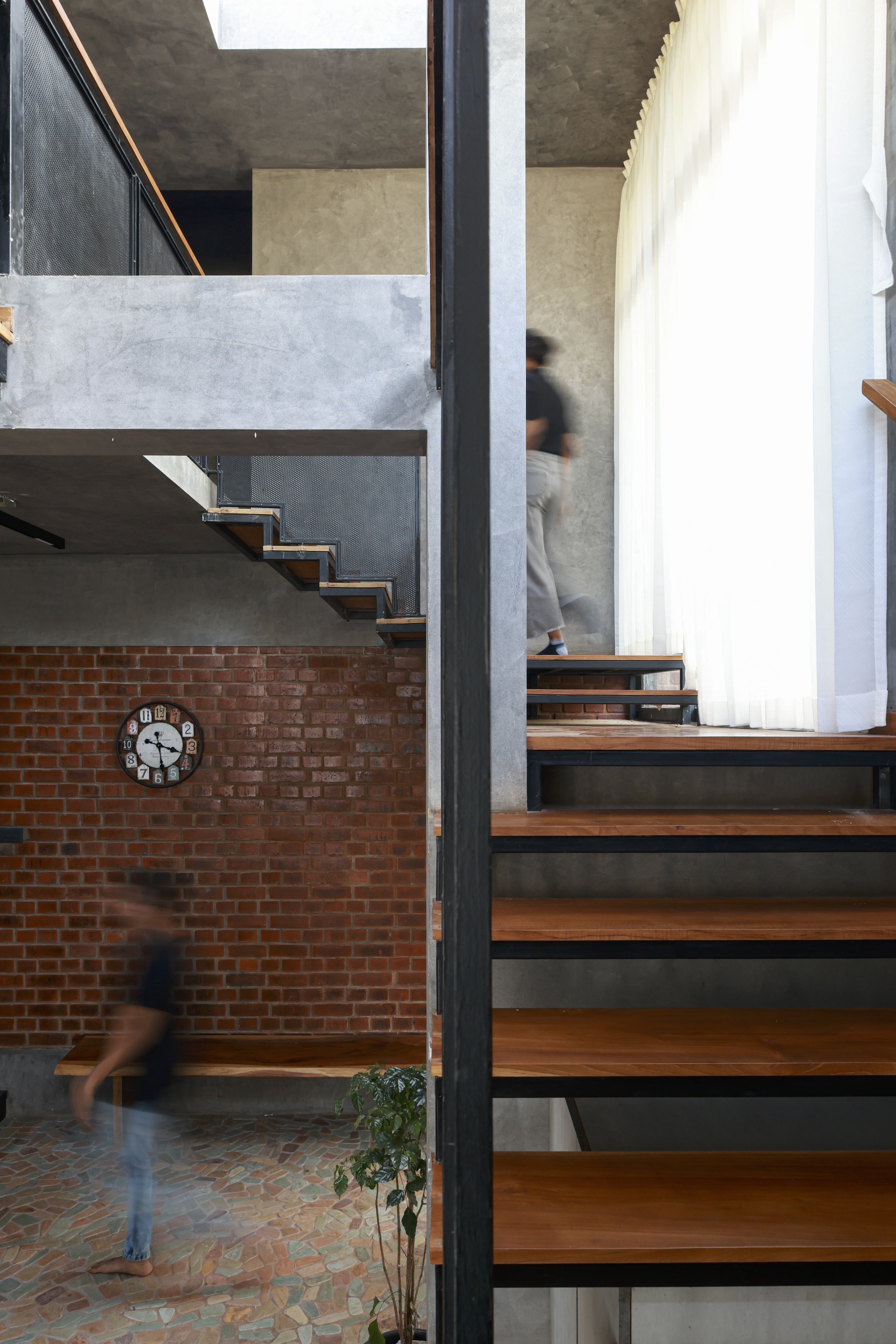 Timber and steel staircase bridging exposed brick wall and concrete landing with figures in motion below
