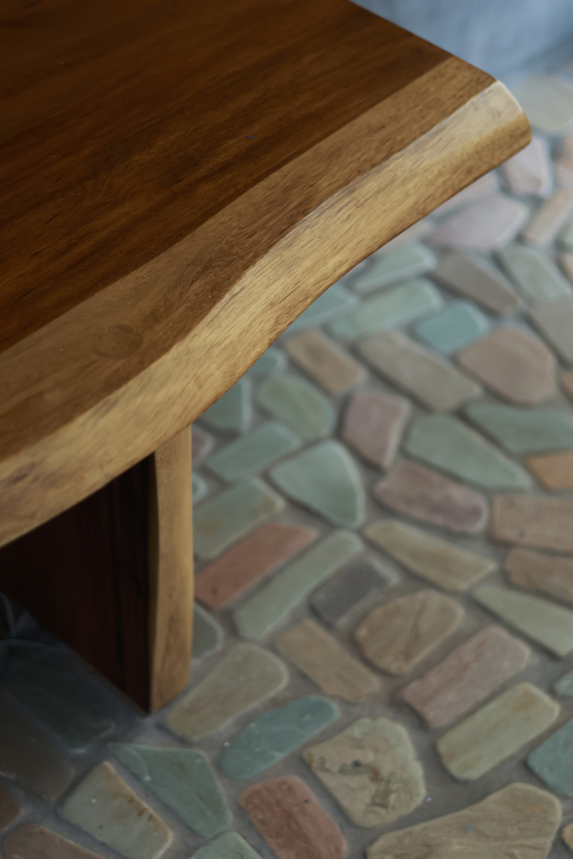 Close-up of rounded timber table edge above patterned pebble floor in pastel tones