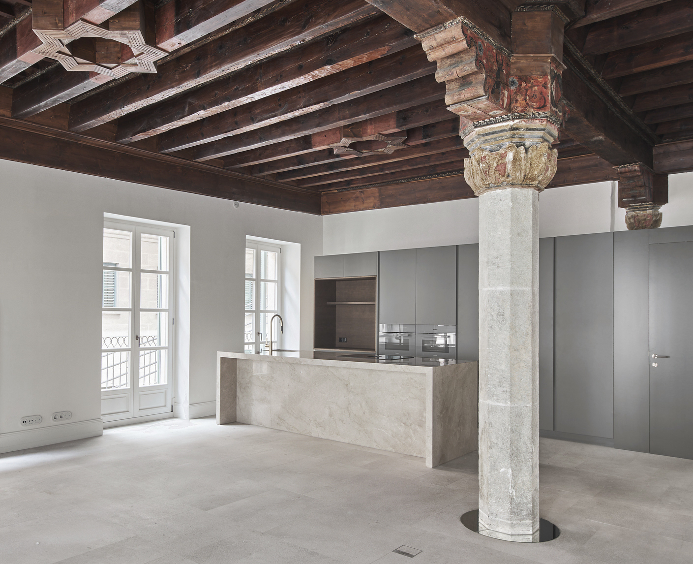 Open kitchen with marble island and grey cabinetry beneath exposed timber beams and an ornamental stone column