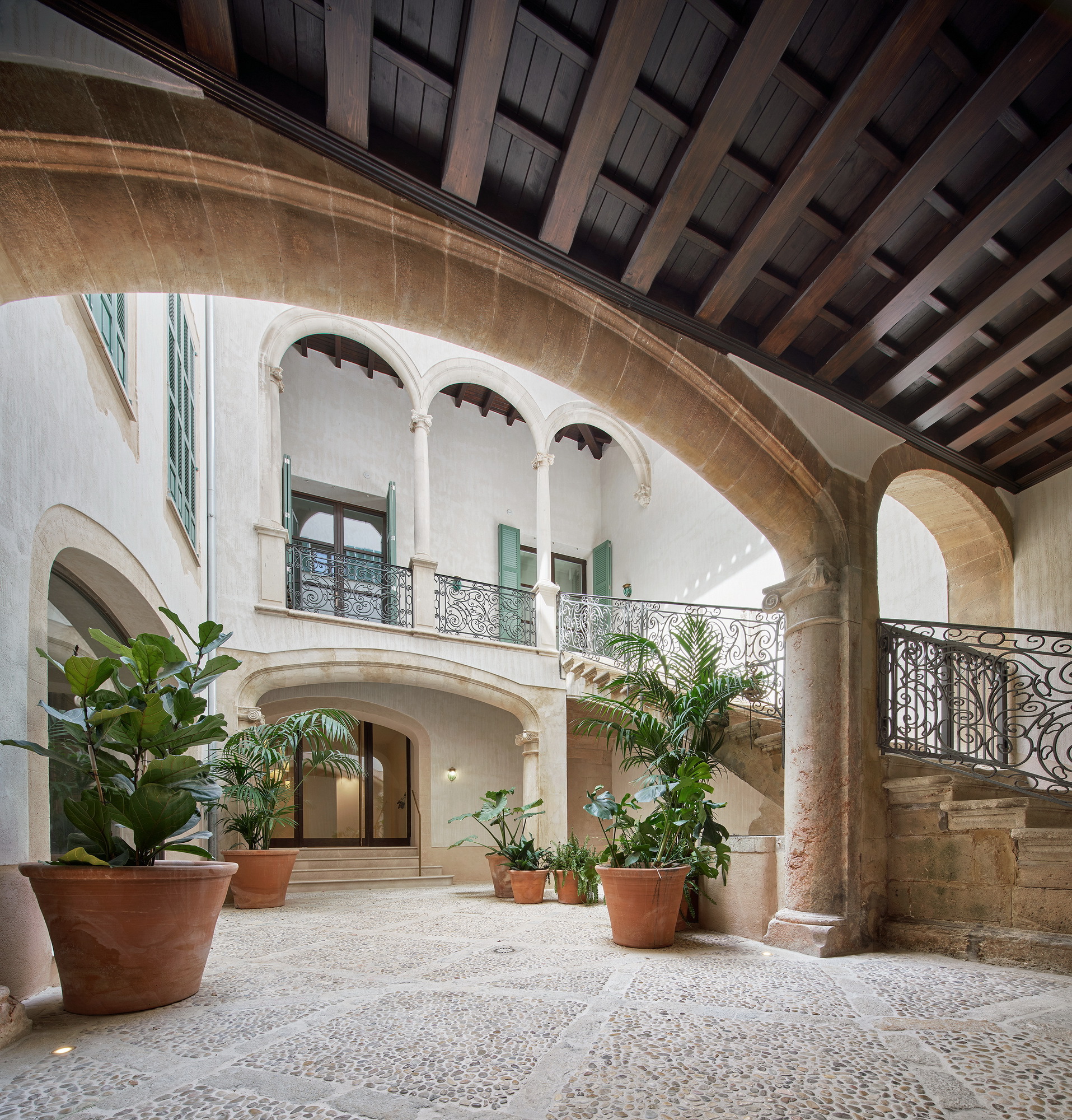 Interior courtyard with pebble mosaic flooring, potted palms and curved stone archway under coffered timber ceiling