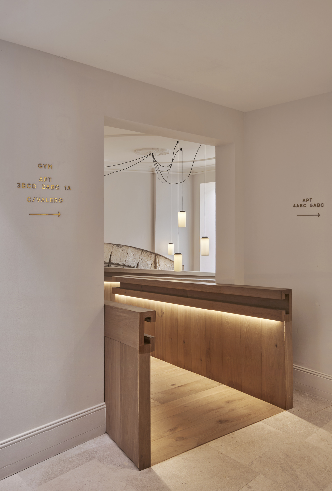 Reception desk of timber with integrated lighting below multi-drop pendant lights and directional signage