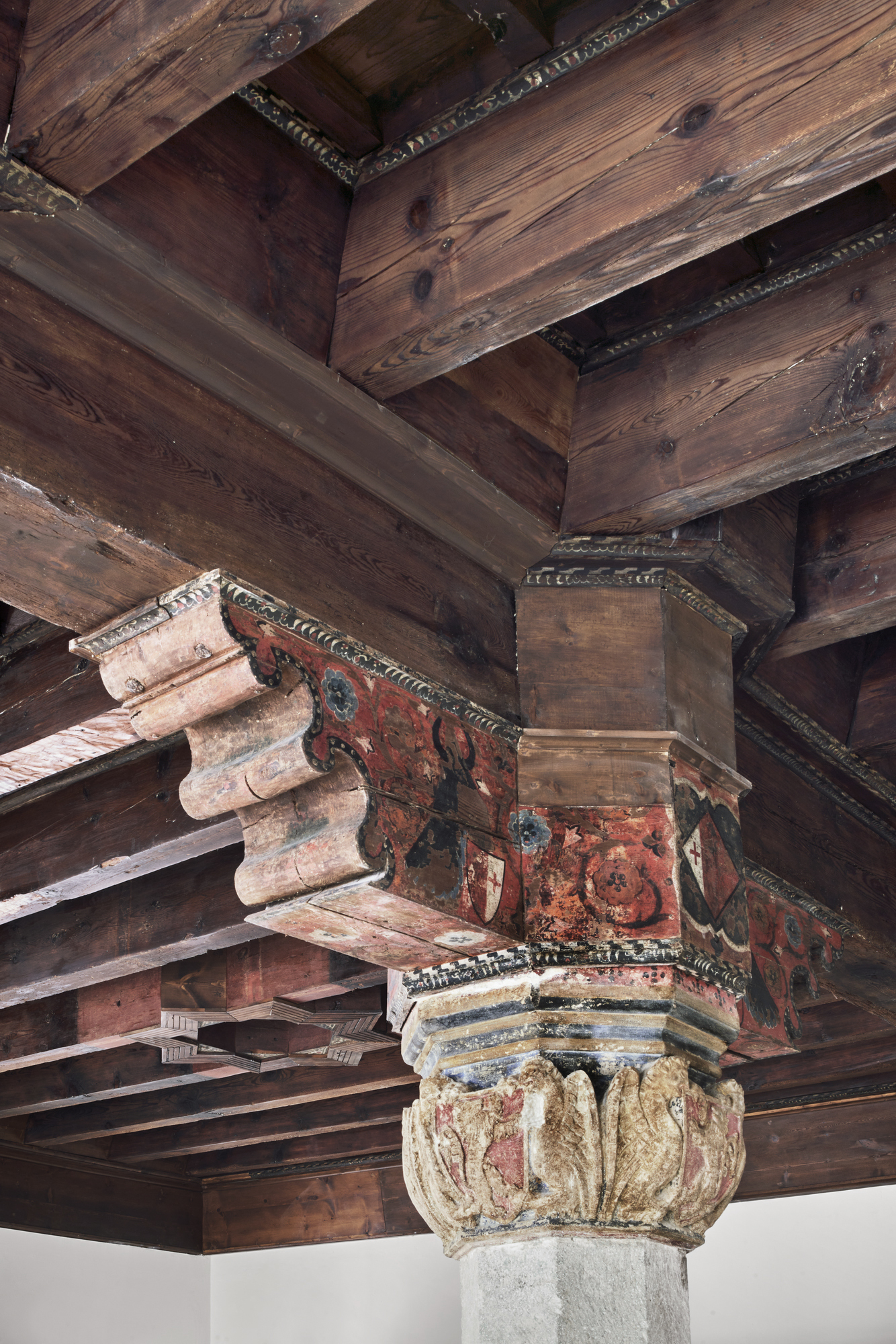 Close-up of painted timber capital with red and blue motifs supporting dark wooden ceiling beams