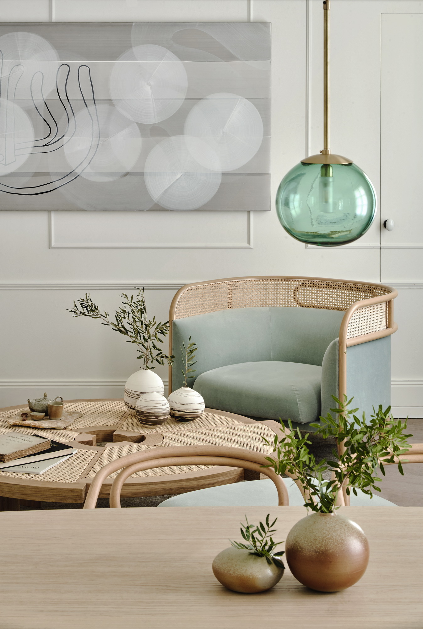 Caned armchair with pale green upholstery beneath a teal glass pendant light and white paneled wall