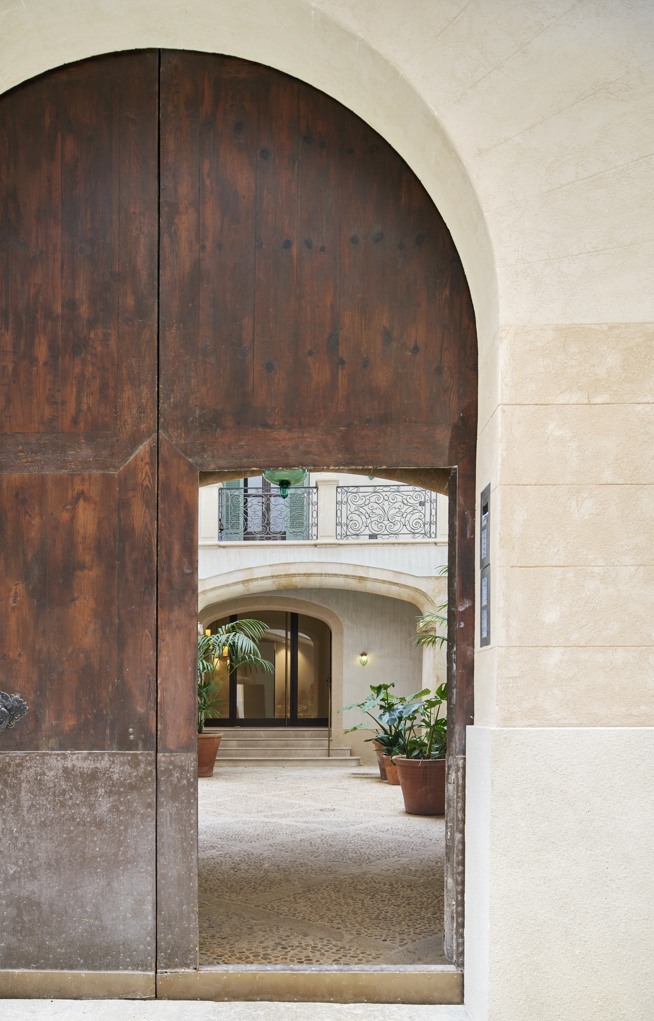 Arched timber door opening into a stone courtyard with potted plants and wrought iron balcony above