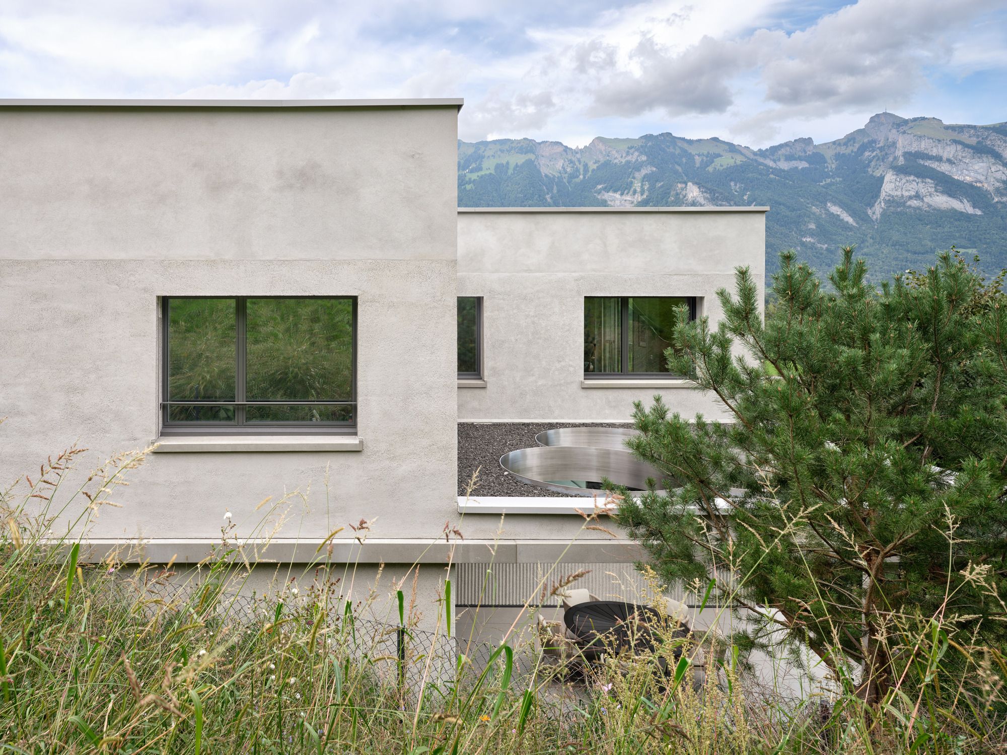 Stepped terraces with horizontal windows framed by fluted cladding beneath a mountain range under cloudy skies