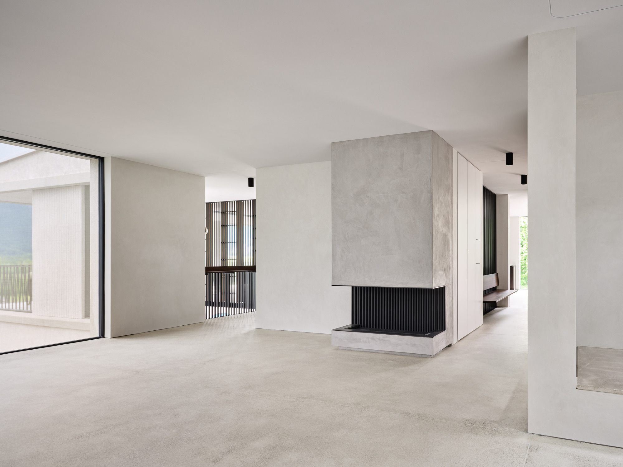 Open living space with concrete fireplace clad in black fluted metal and pale stone flooring throughout