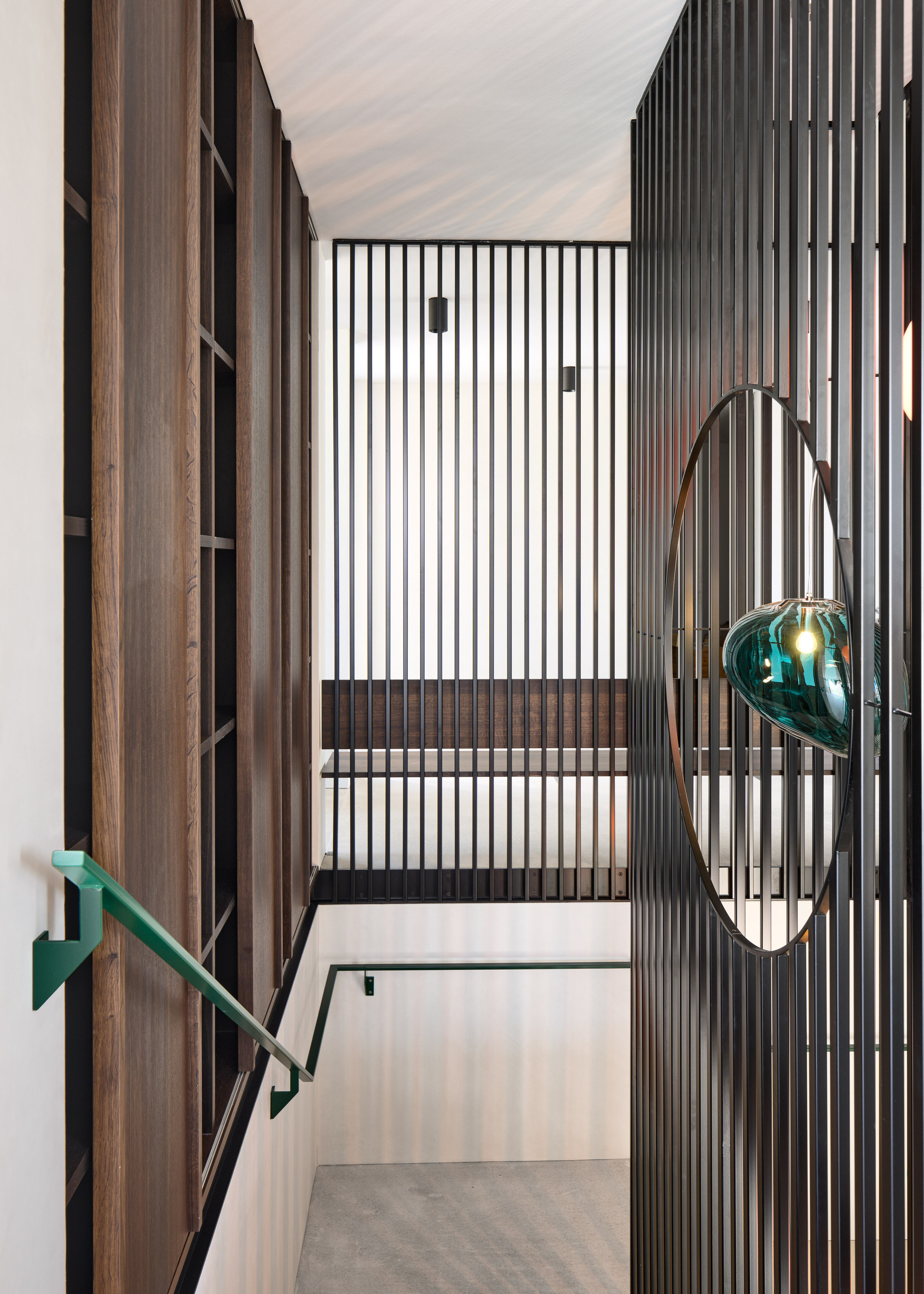 Stairway landing with vertical timber slats and suspended green glass light fixture in daylight