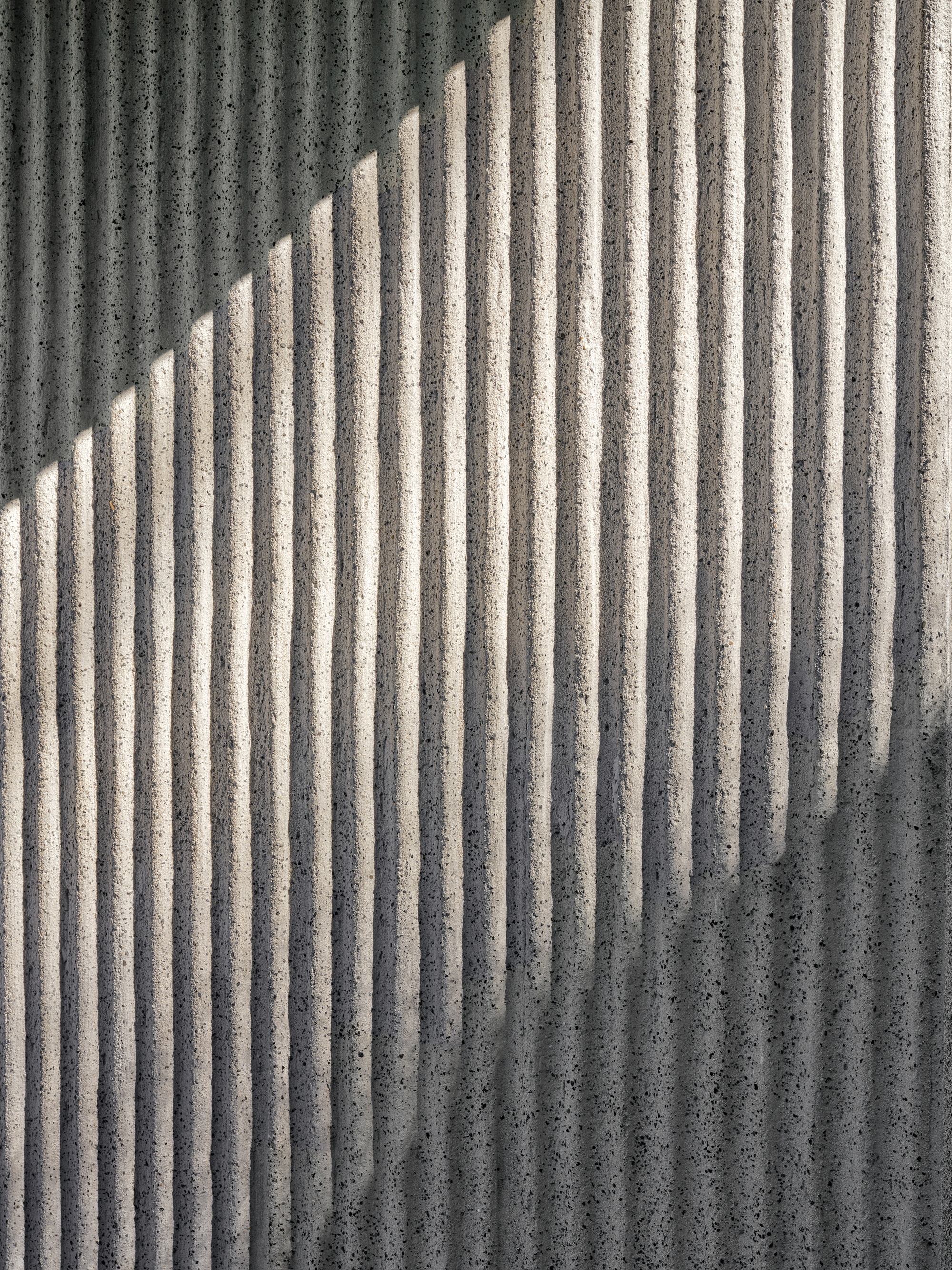 Close-up of ribbed concrete surface with diagonal shadow pattern cast across vertical grooves