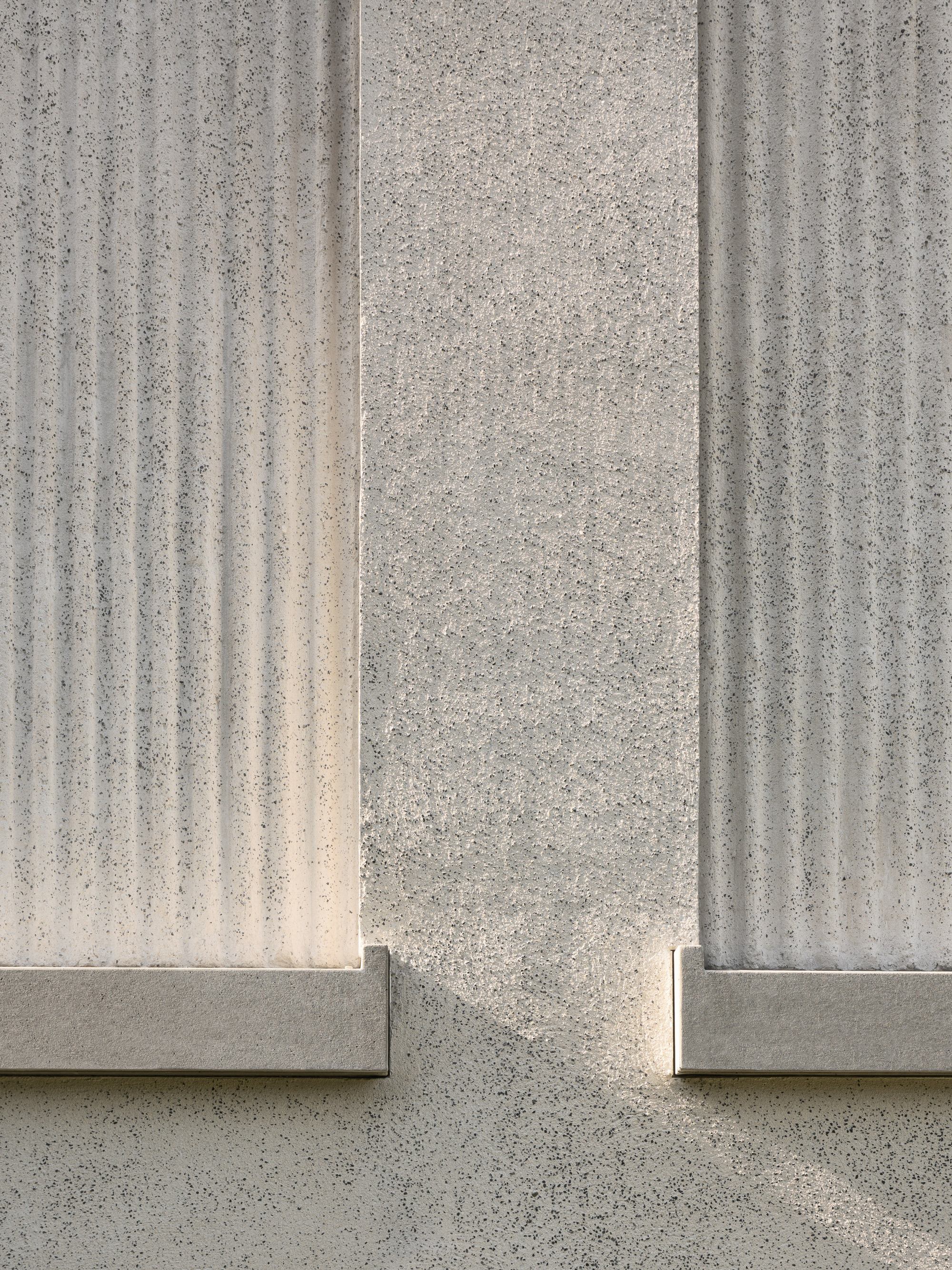 Close-up of vertically fluted concrete panels meeting at a corner joint in bright sunlight