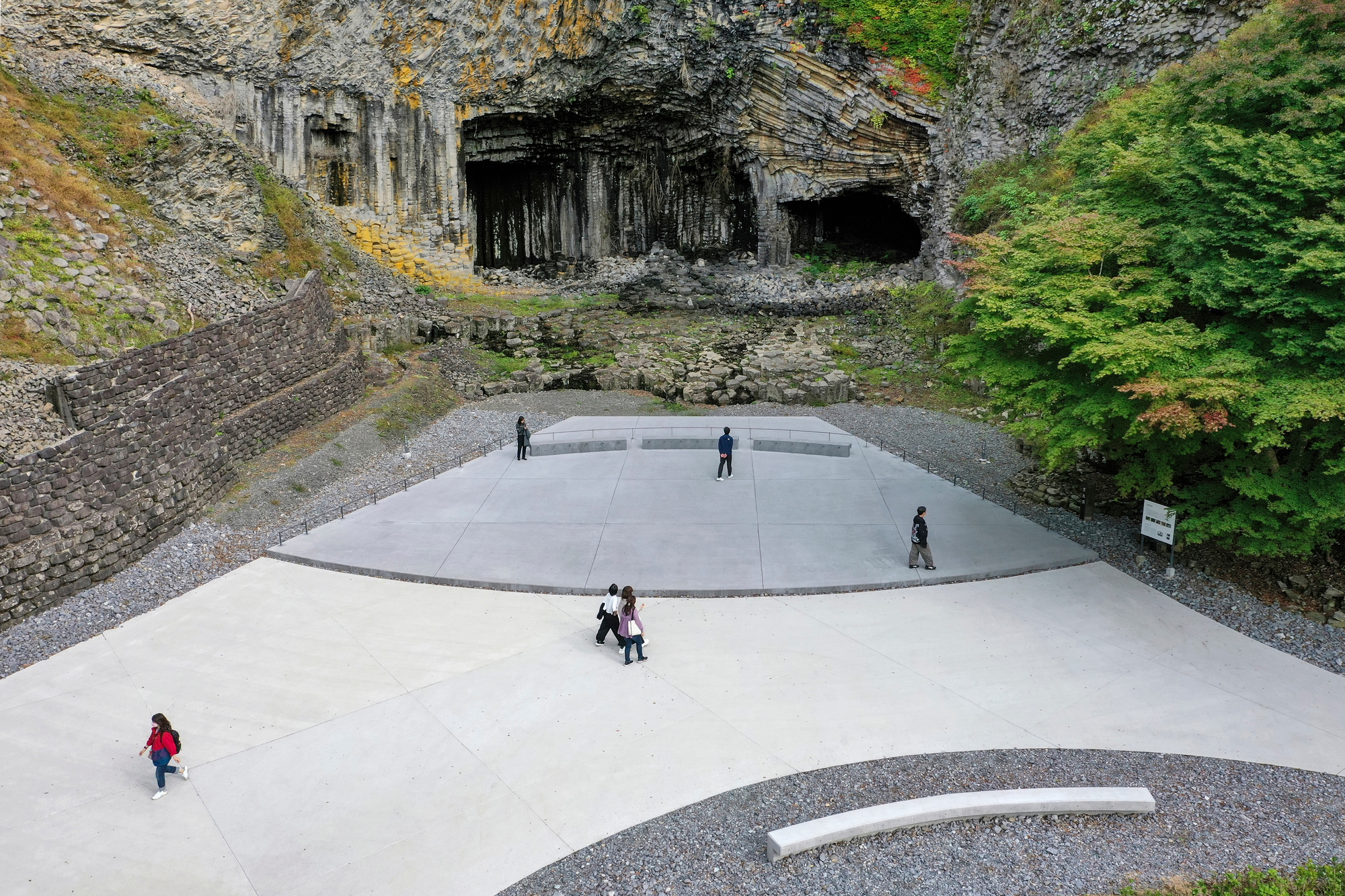 Aerial view of the curved concrete plaza with visitors scattered across its surface below a basalt cliff