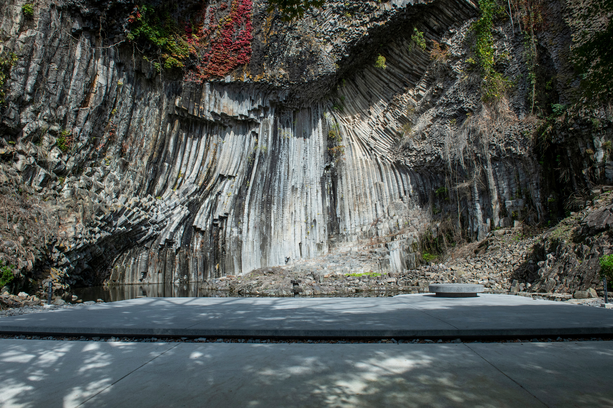 Concrete platform at the base of vertical basalt columns with a circular opening in the pavement
