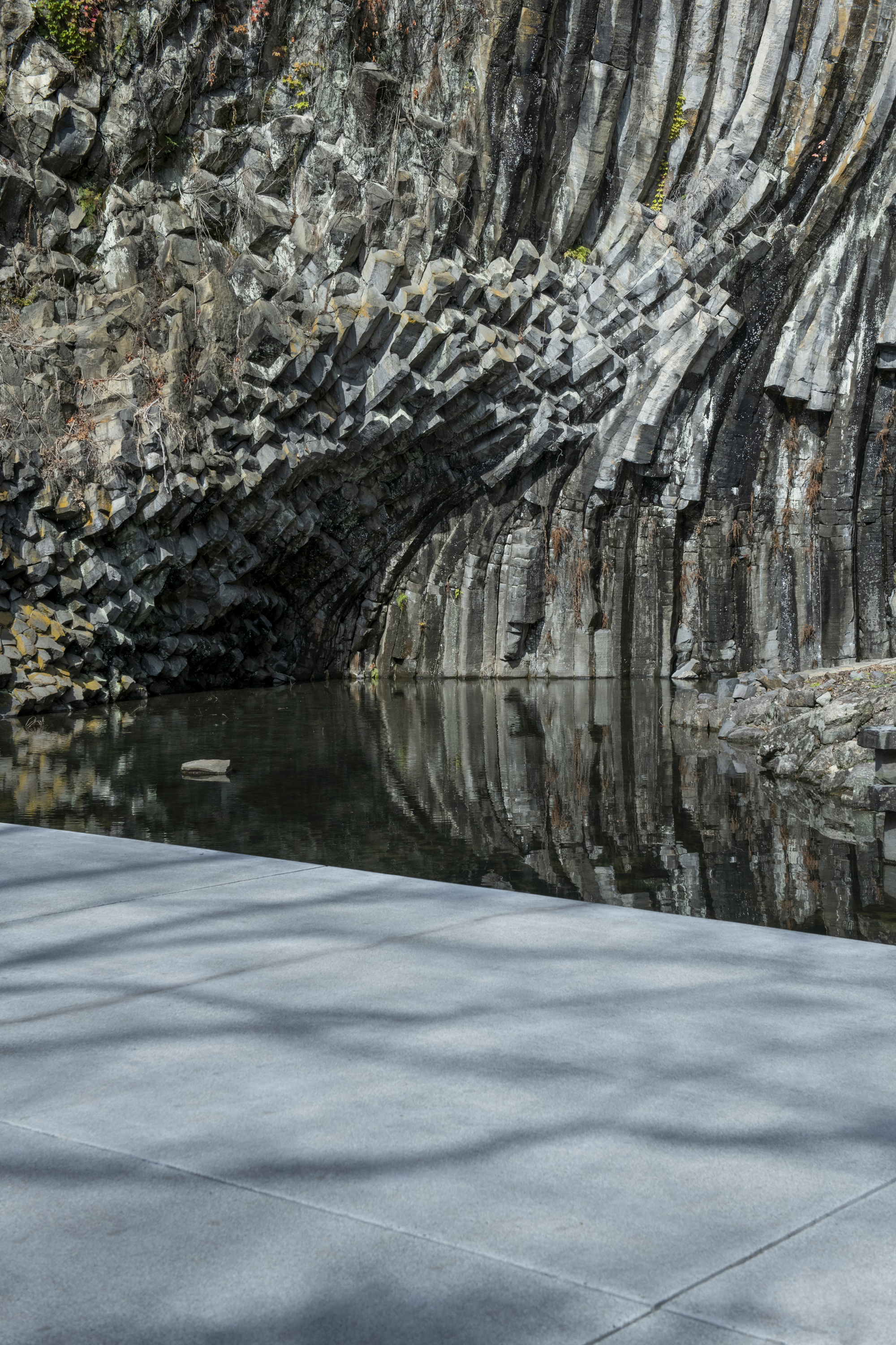 Concrete roof edge meeting the fractured basalt cliff face above a reflecting pool