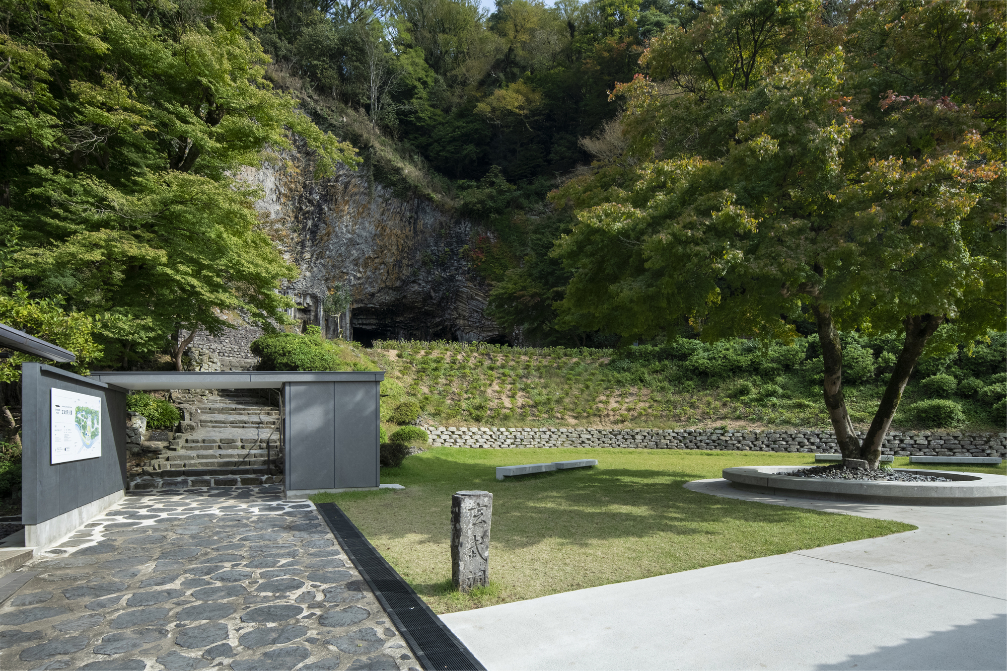Entry pavilion with dark metal cladding and timber screen facing a lawn and stone retaining walls