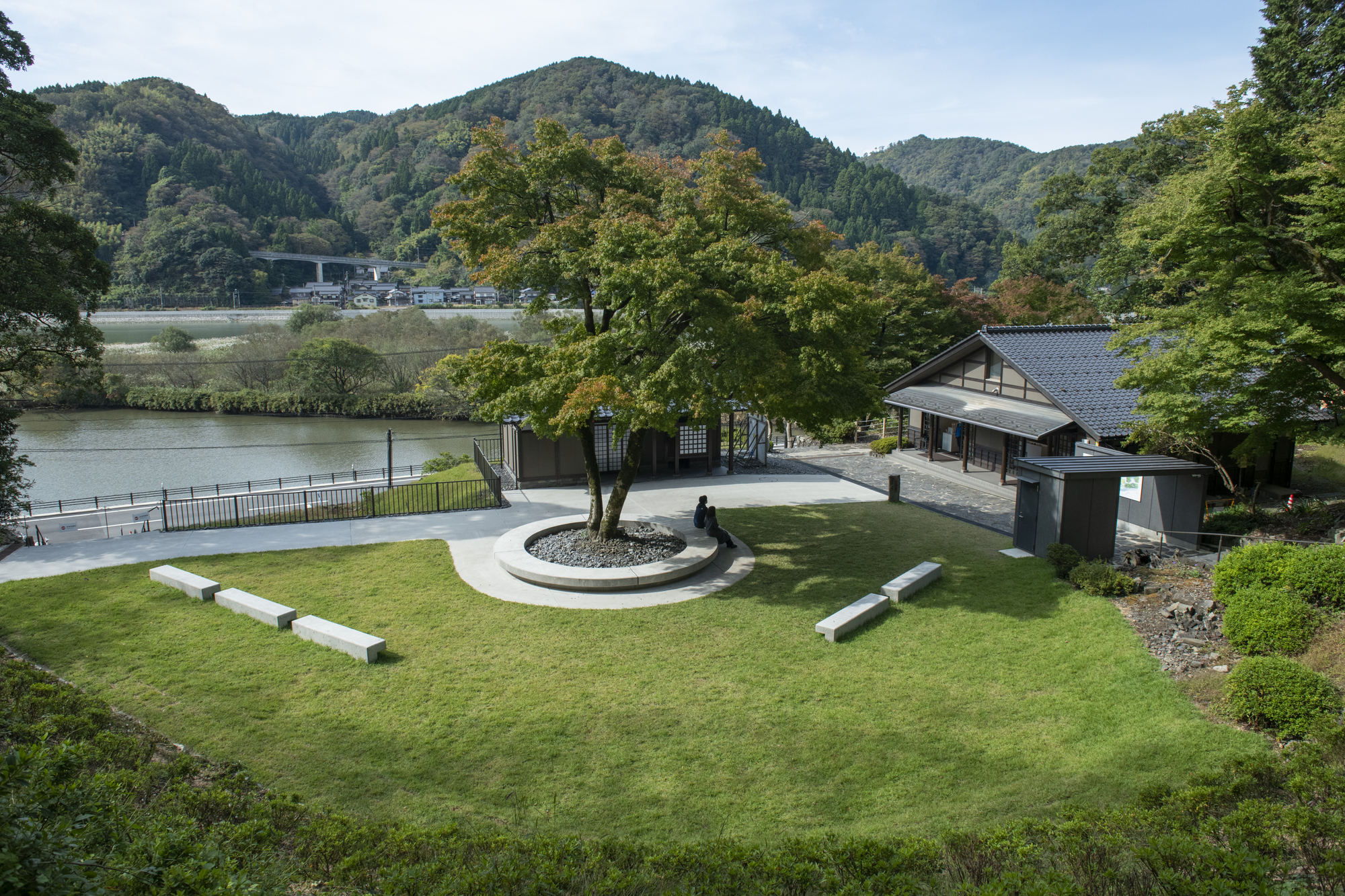 Overview of the lawn with circular tree planting and concrete benches overlooking a river valley