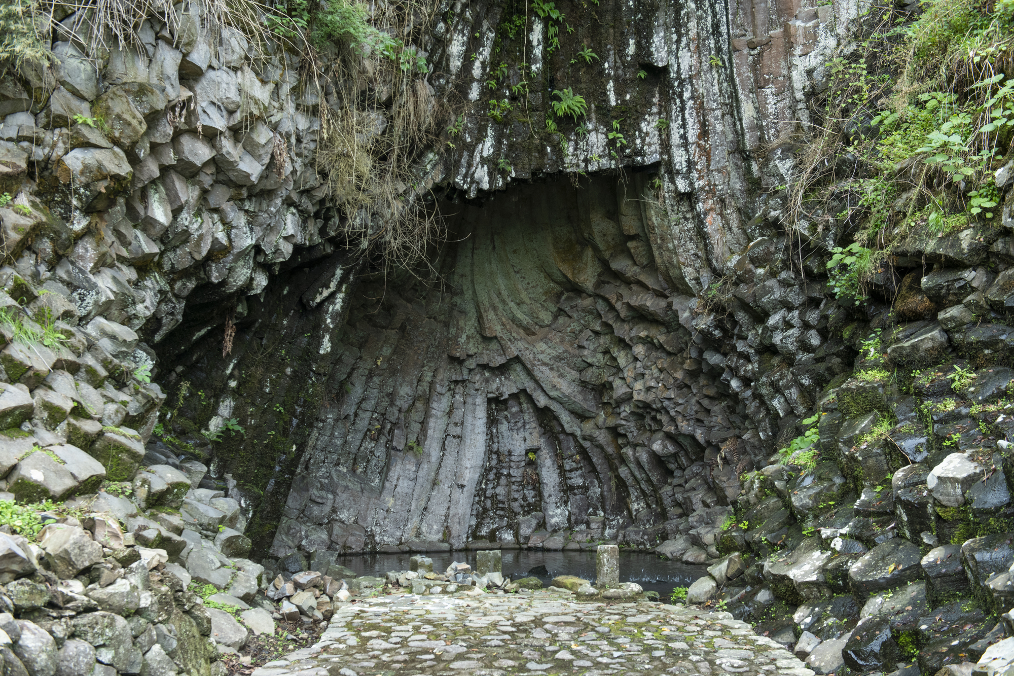 Stone grotto entrance with hexagonal basalt columns framing a vaulted ceiling and cobblestone floor