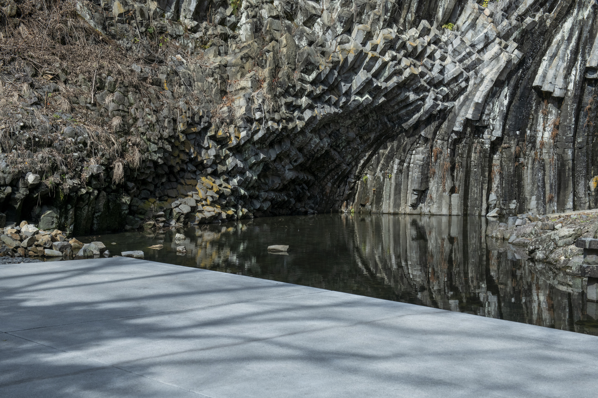 Concrete platform edge meeting a still water pool beneath towering basalt cliff formations