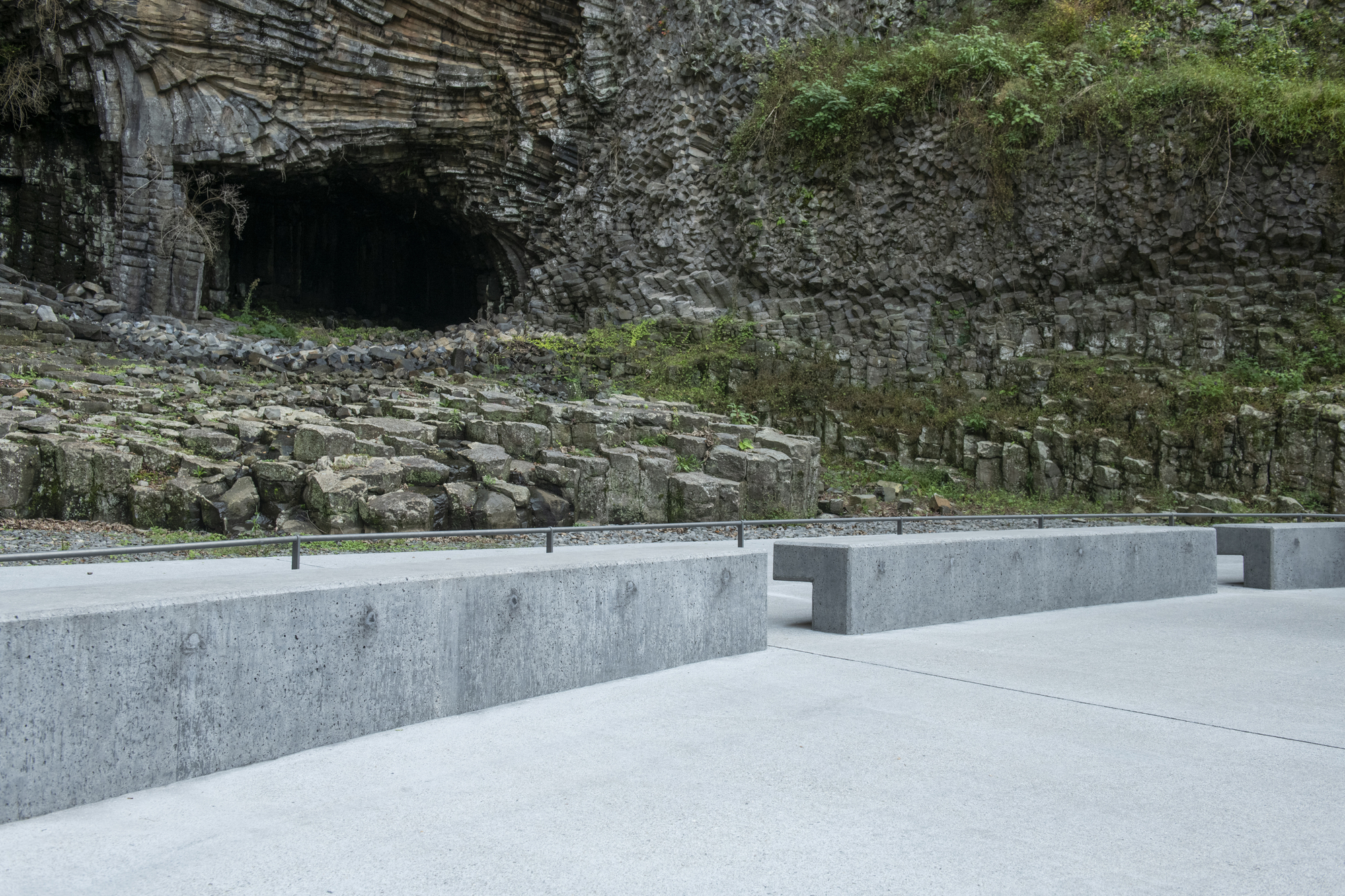 Low concrete wall with integrated bench seating and metal railing facing the columnar rock formation