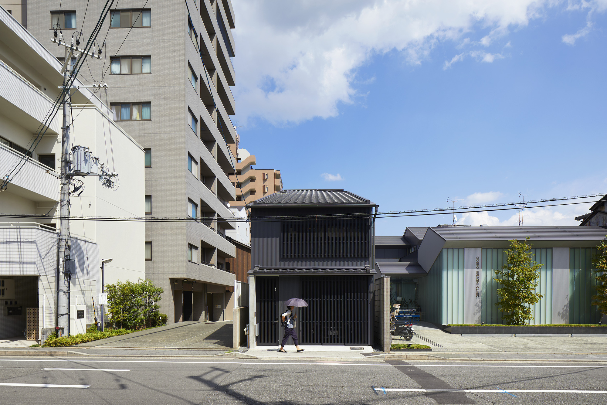 Black slatted facade of a two-storey house nestled between mid-rise apartment buildings under blue sky