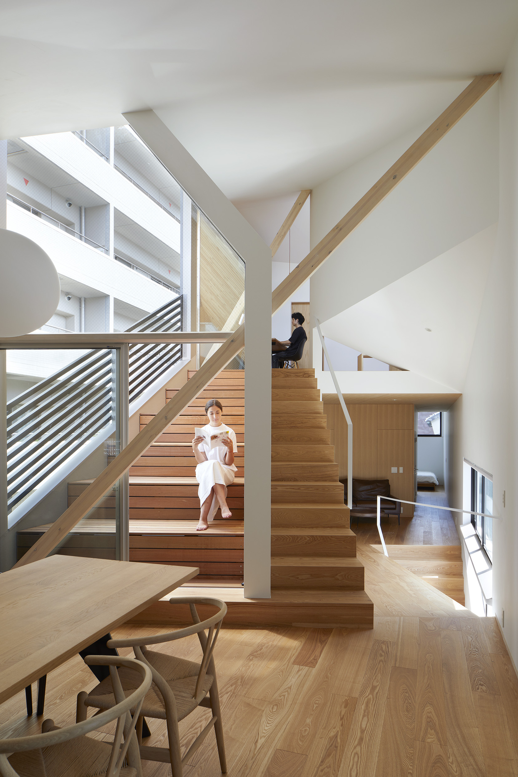 Multi-level timber staircase with diagonal striped railings where two people sit on the steps