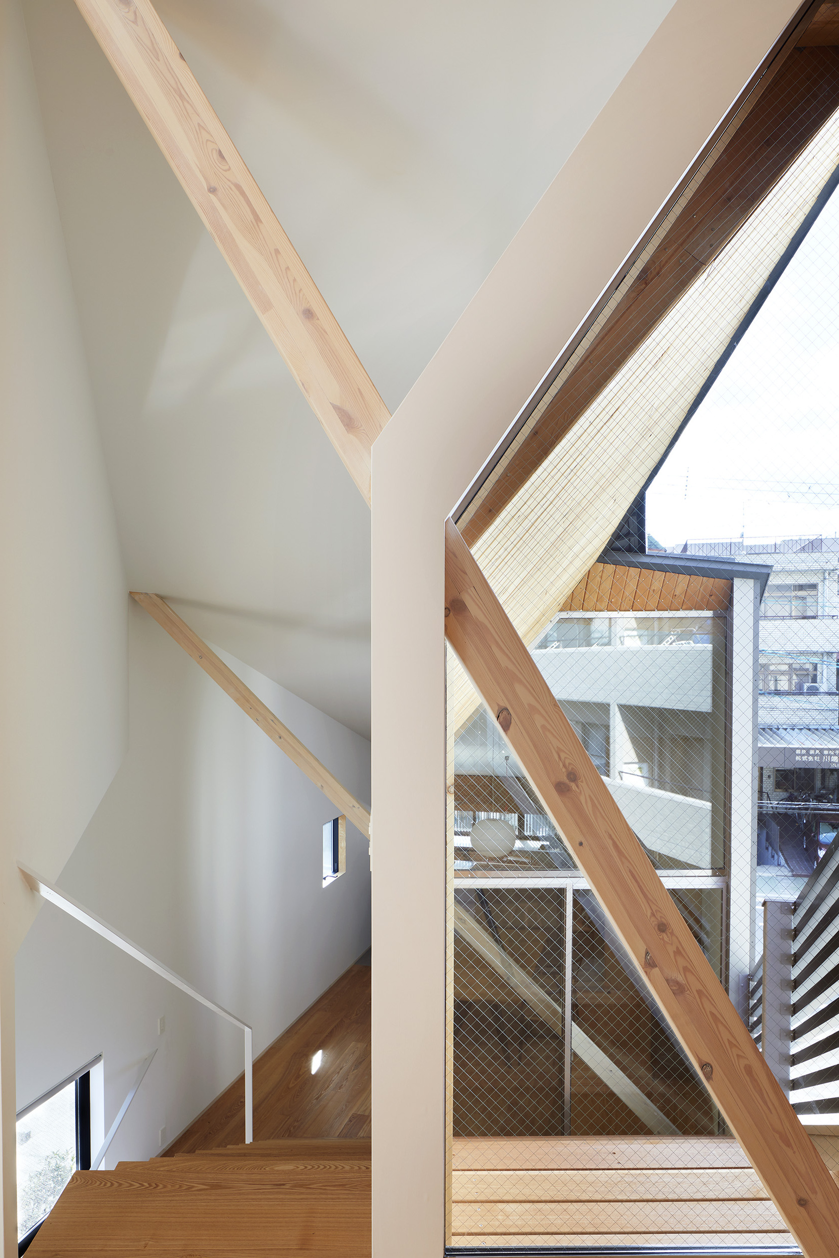 Interior stairwell with exposed timber beams framing glazed openings that reveal neighboring buildings
